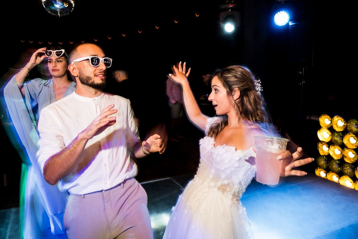Wedding celebration with guests dancing under blue and purple lighting.
