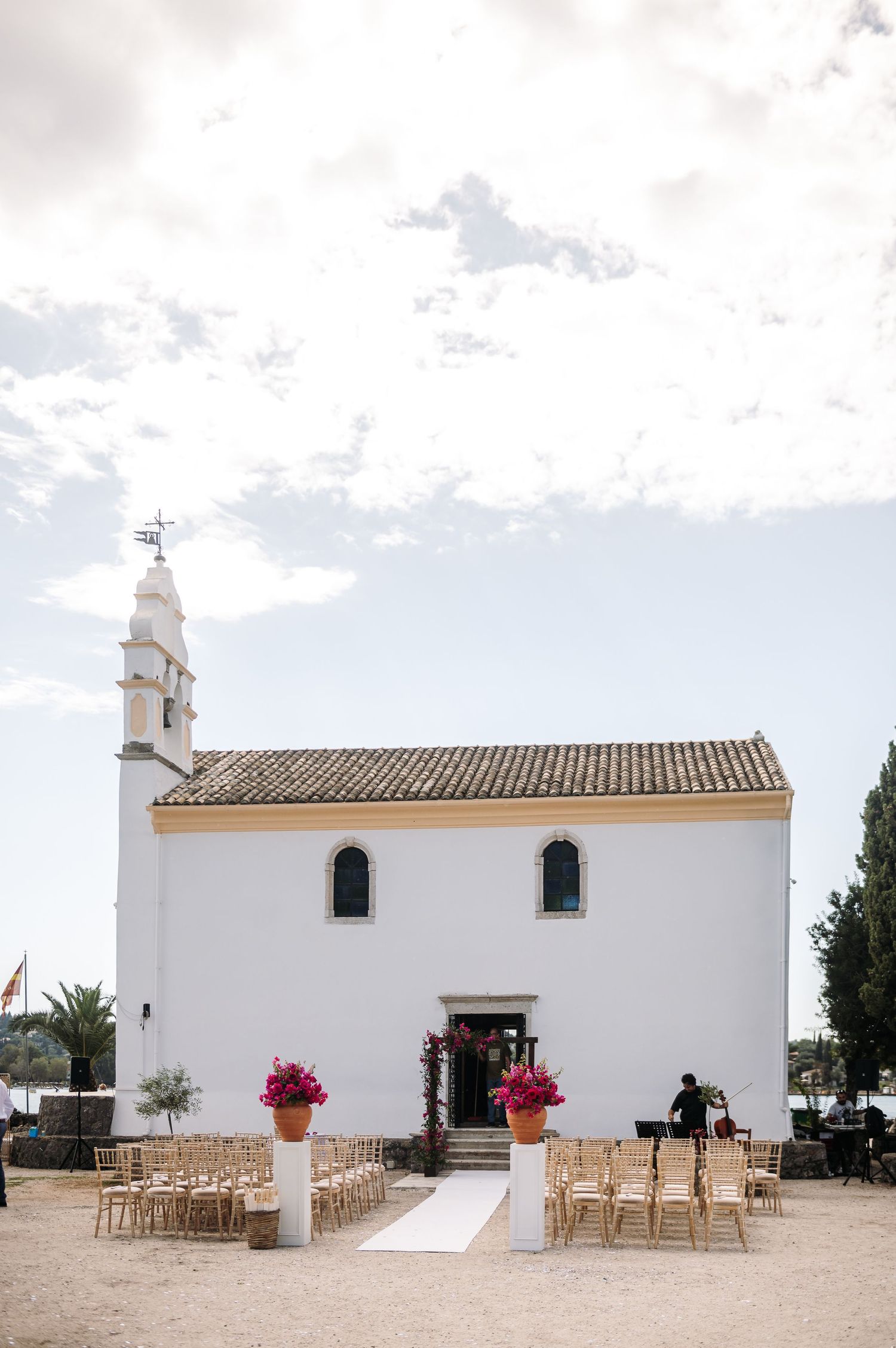 White Mediterranean chapel with wooden chairs set up for outdoor wedding ceremony.
