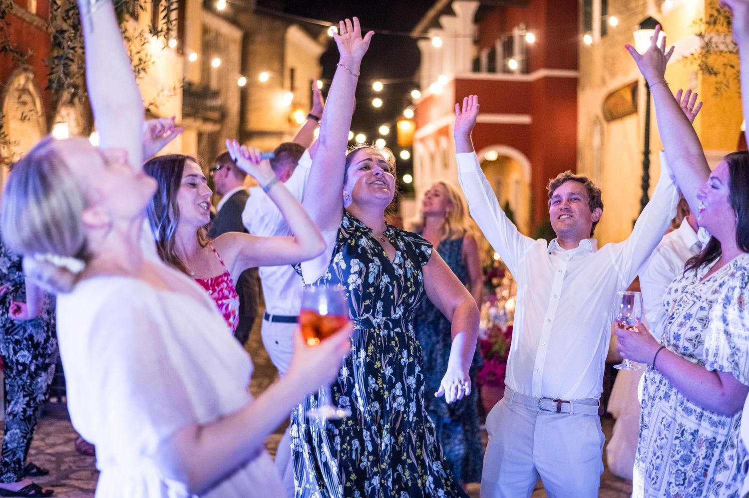 Celebration on dance floor with guests raising hands under string lights.