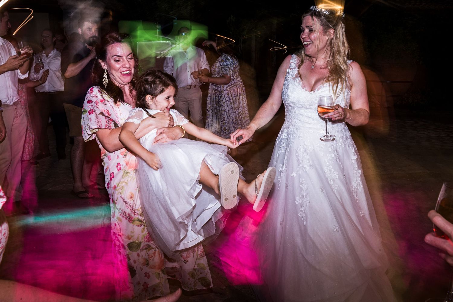 Wedding party dancing under vibrant pink and green lighting effects at a nighttime celebration.