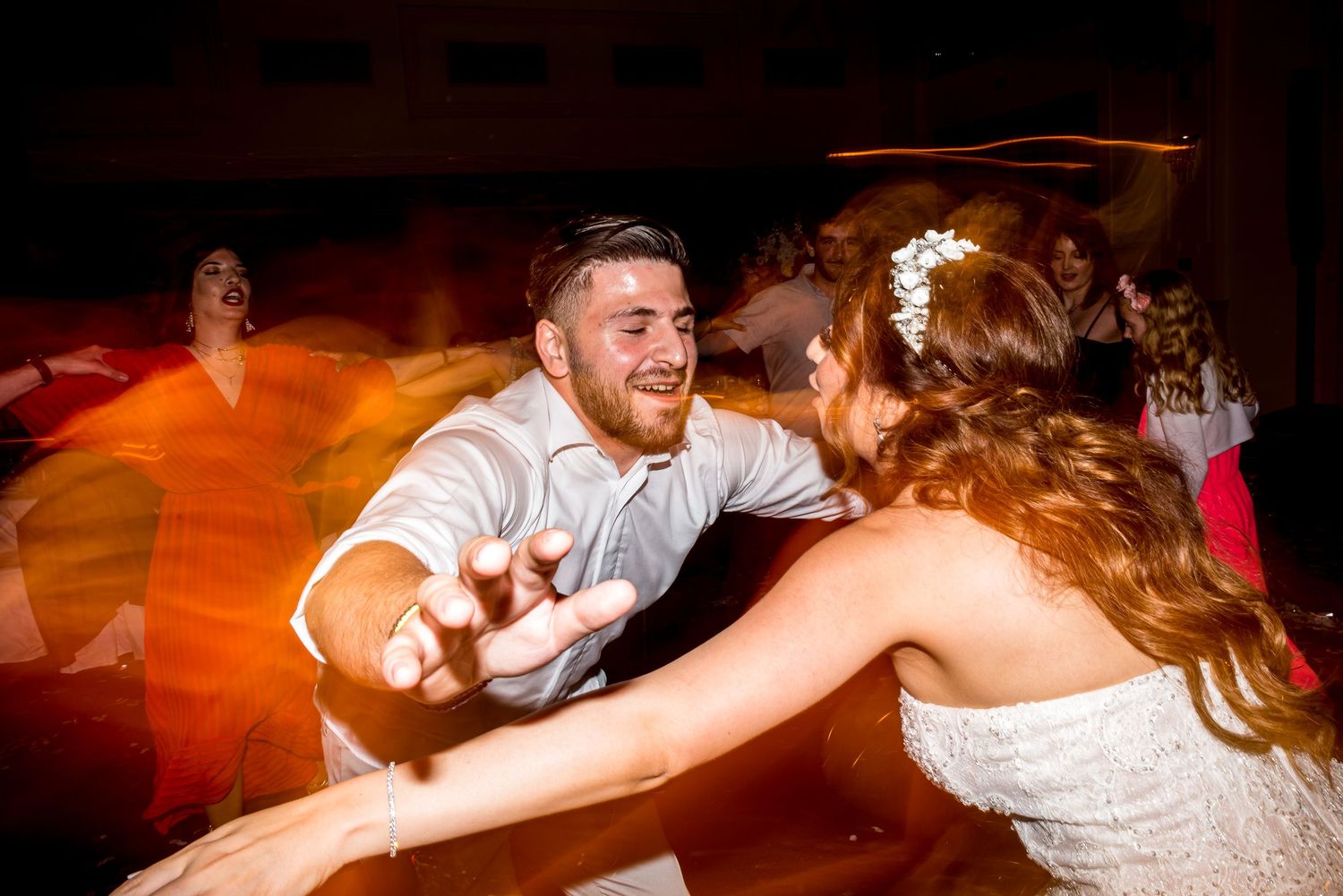 Wedding reception party with guests dancing under warm lighting on a wooden dance floor.