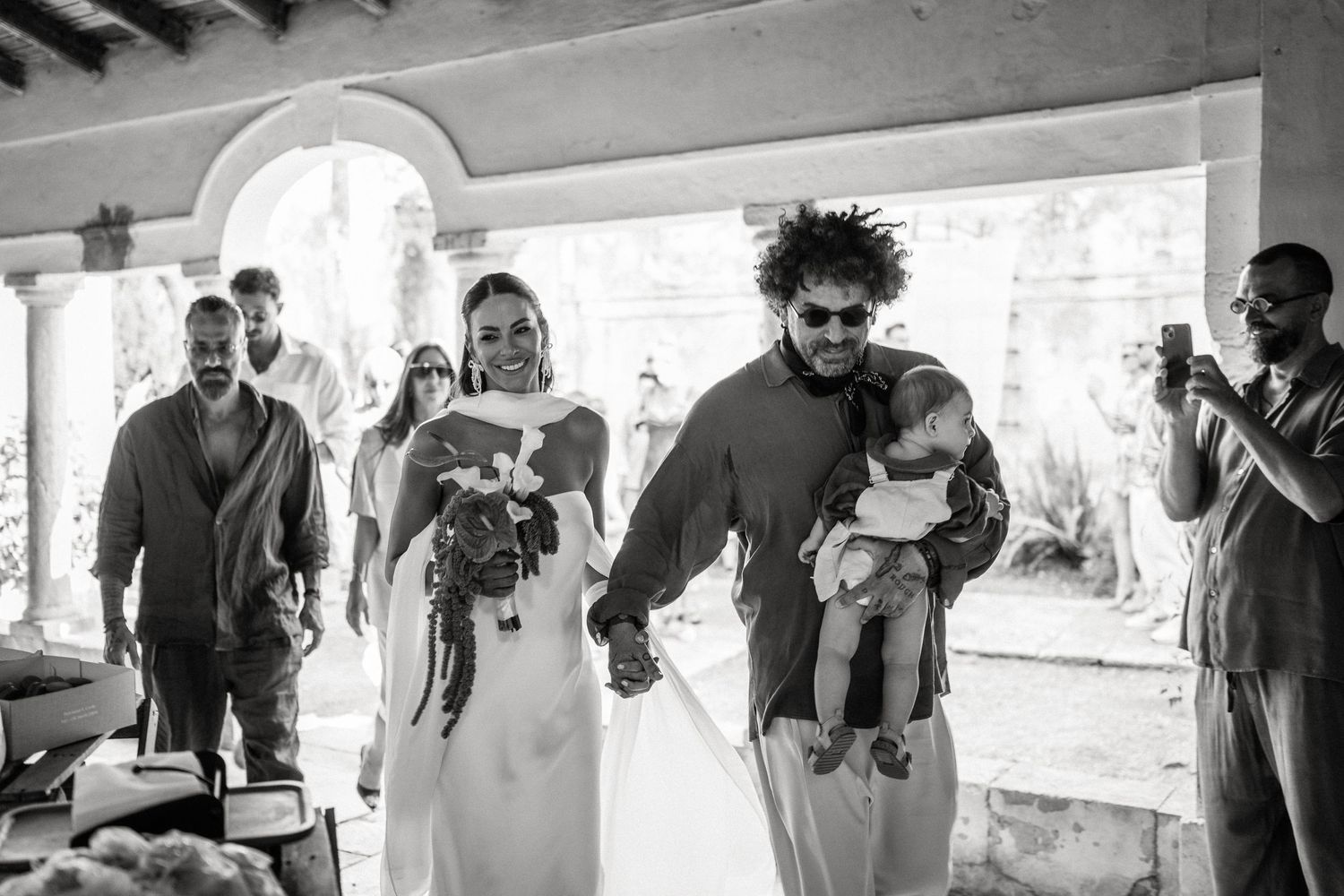 Black and white candid moment from wedding celebration under arched walkway.