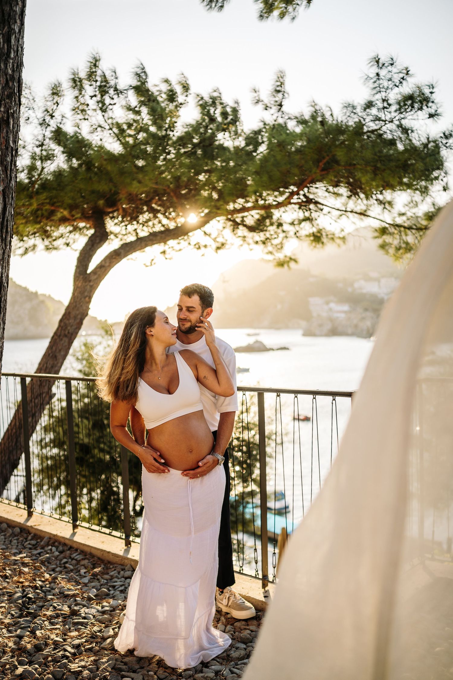 Couple in white clothing dances together on a terrace overlooking the Mediterranean sea at sunset.
