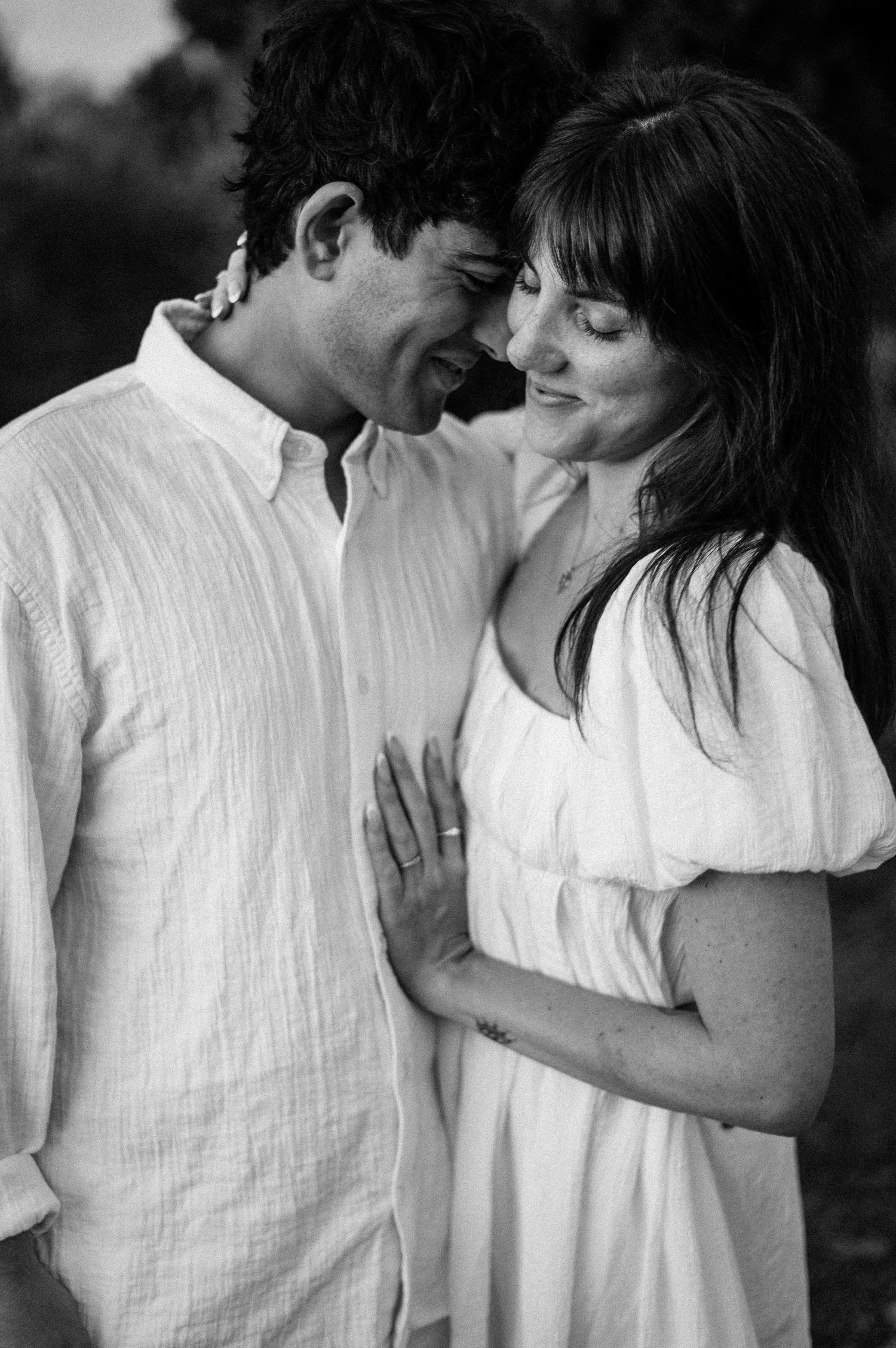 A tender black and white moment between a couple in white clothing against a natural backdrop.