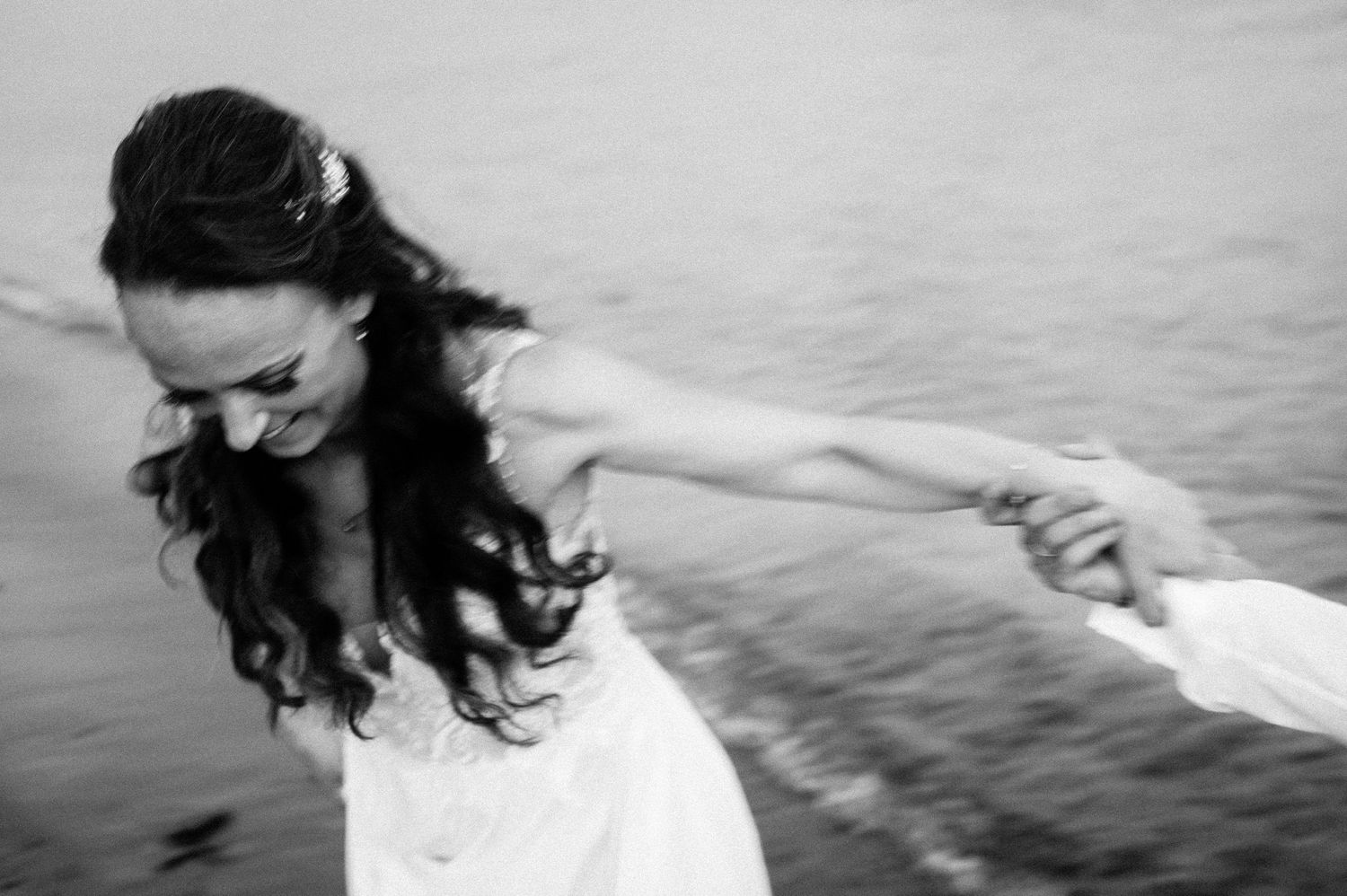 Bride in flowing white dress twirls joyfully by the ocean waves.