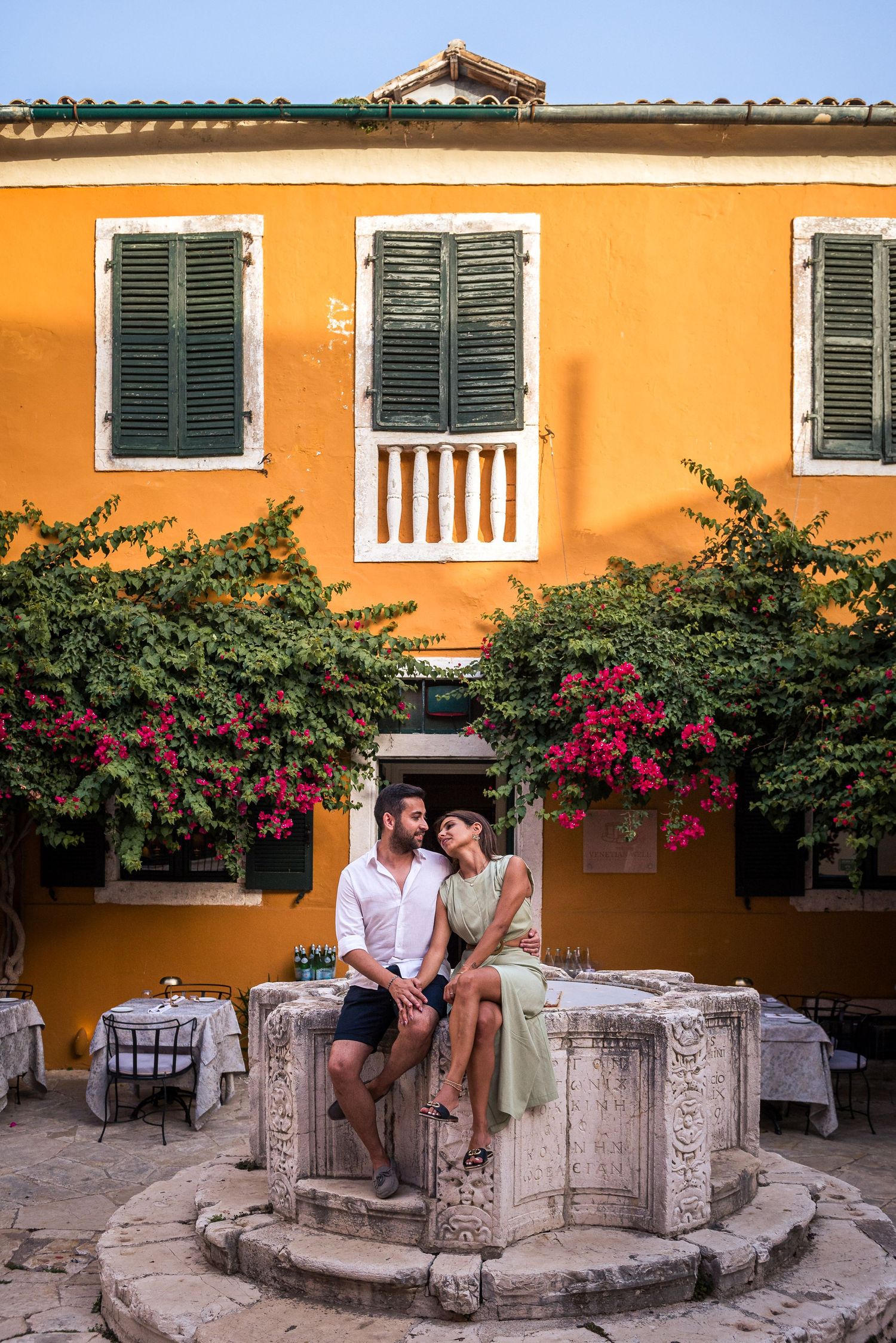 Mediterranean courtyard with orange walls, green shutters, and pink bougainvillea flowers.