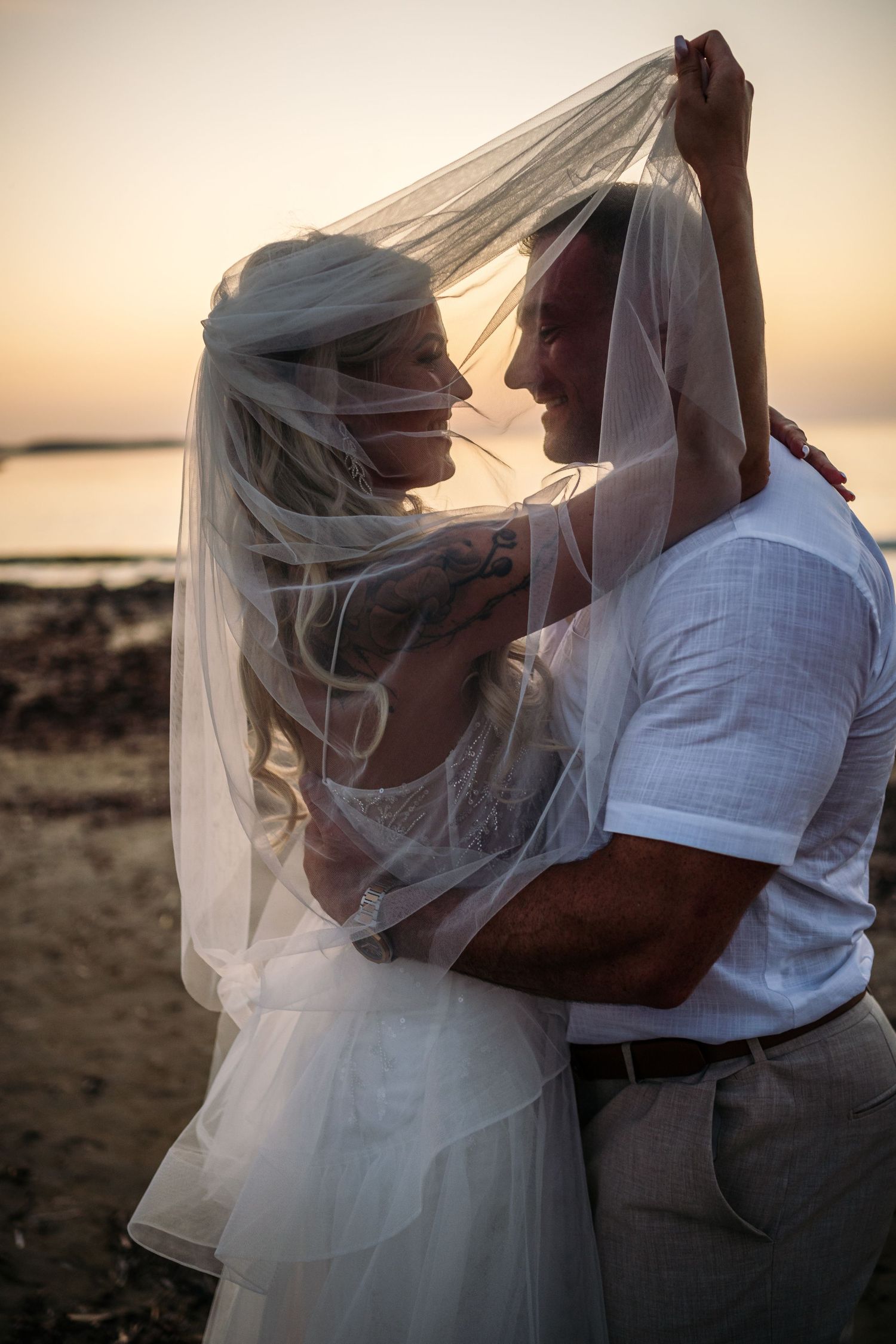 Sunset beach wedding photos with flowing veil creating romantic atmosphere.