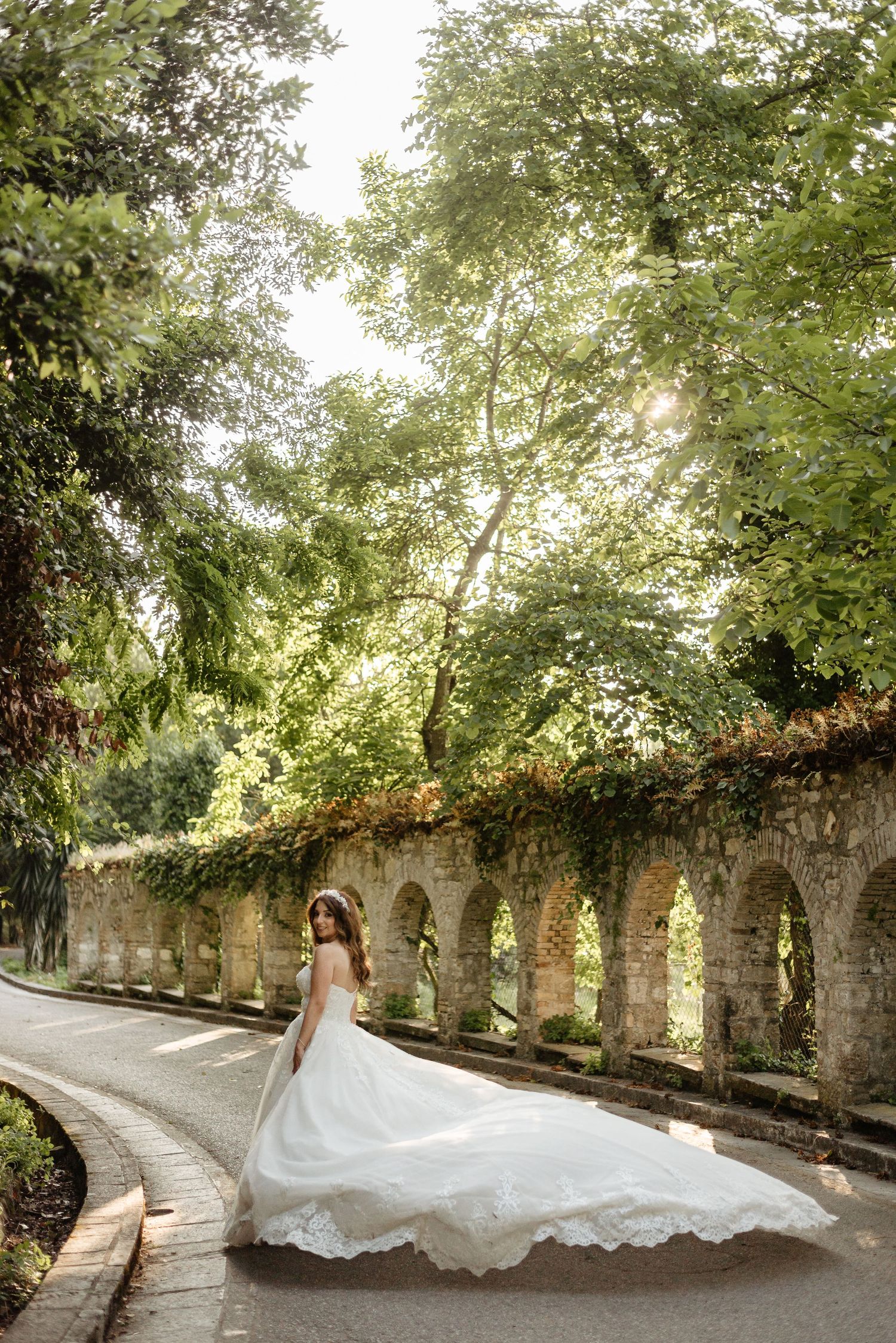 Bride's dress flows dramatically along a tree-lined stone pathway.