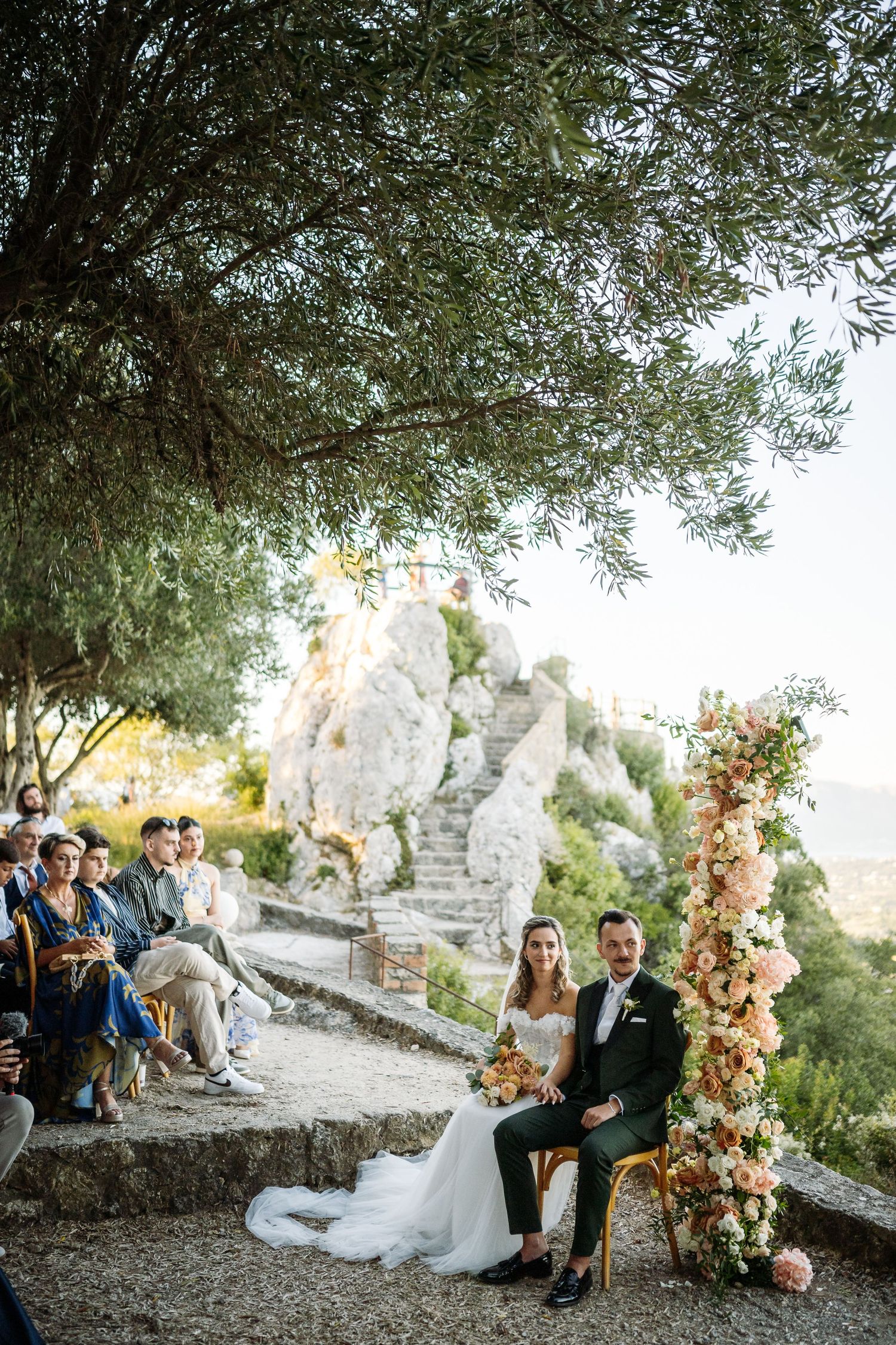 Elegant wedding ceremony setup with floral arch against stone ruins and mountain backdrop.