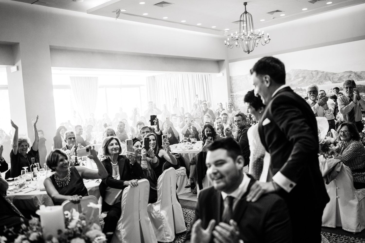 Wedding reception guests cheer and celebrate in an elegant white-decorated ballroom.