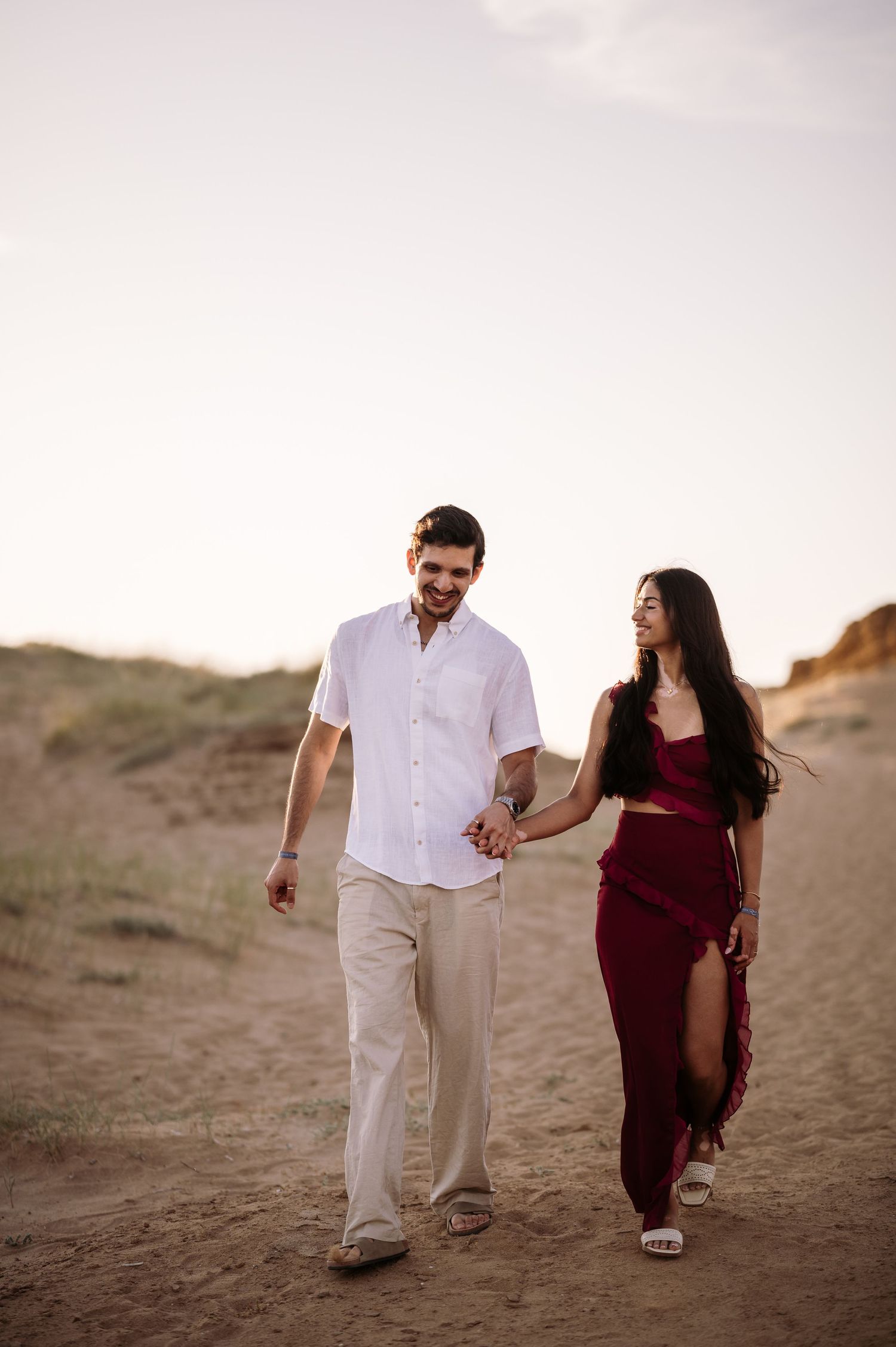 A couple walking hand in hand along sandy dunes during golden hour.