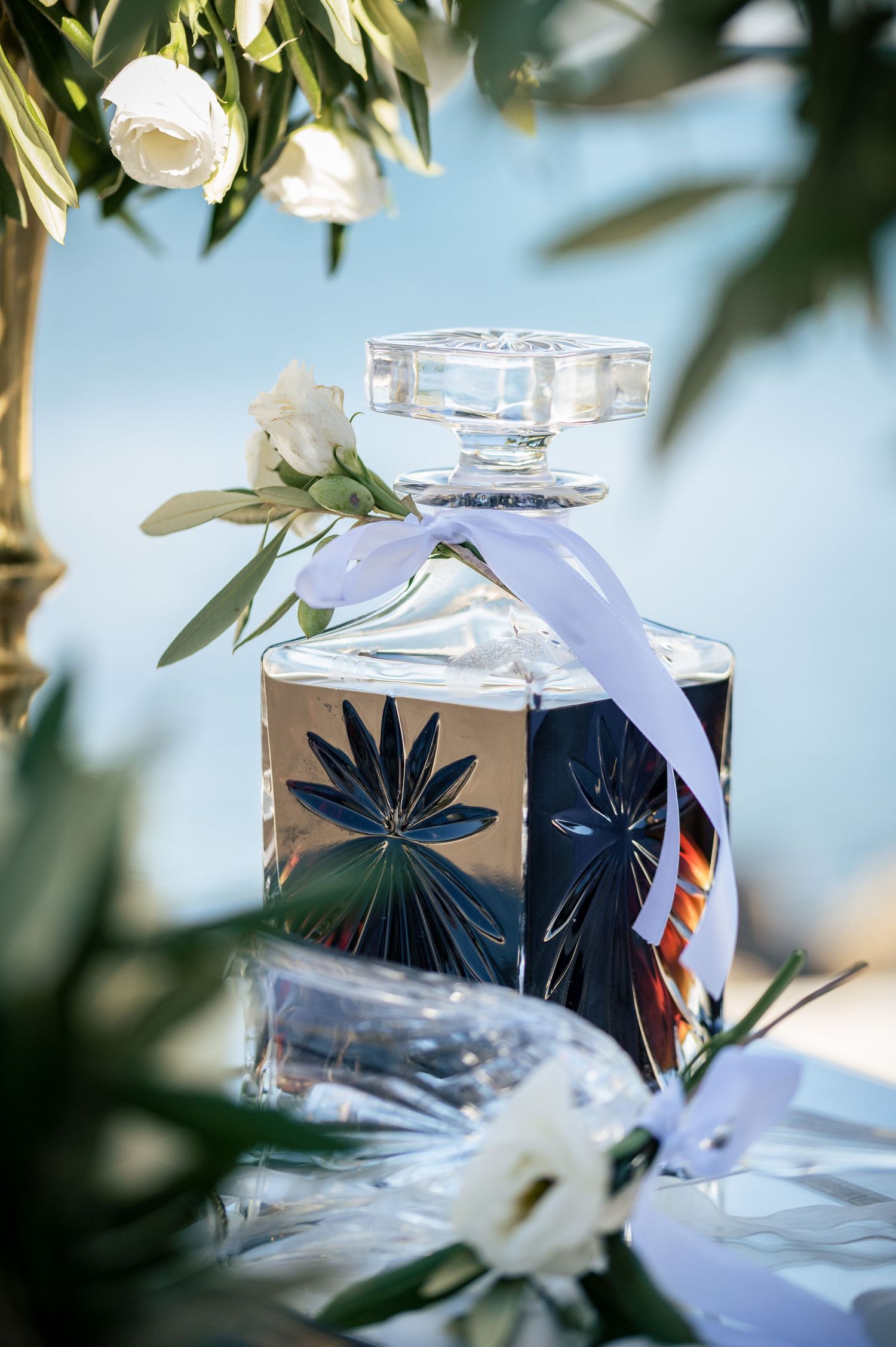 Decorative perfume bottles with white ribbons arranged among green foliage.
