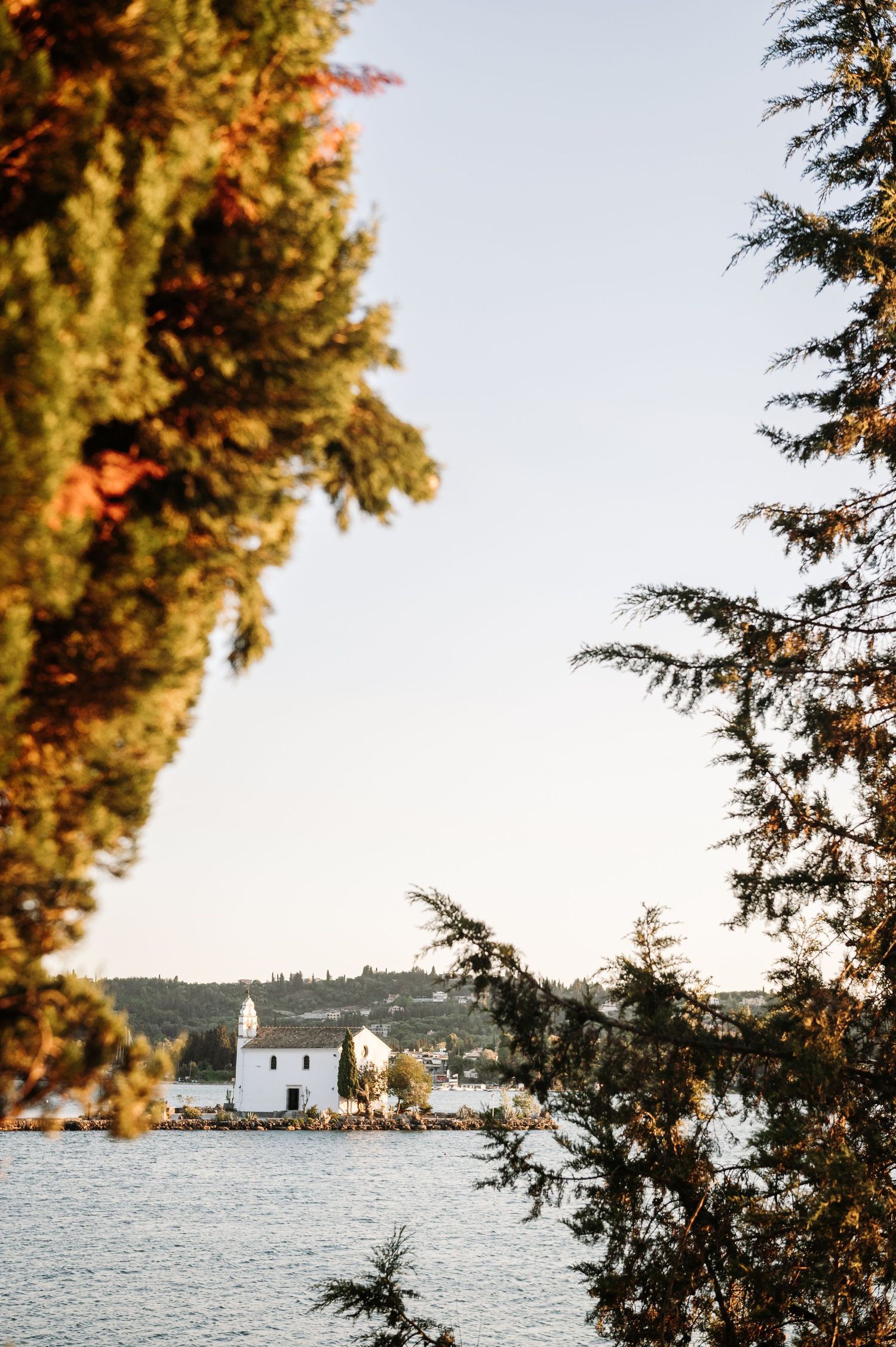 A white church sits on a small island surrounded by blue waters and cypress trees.