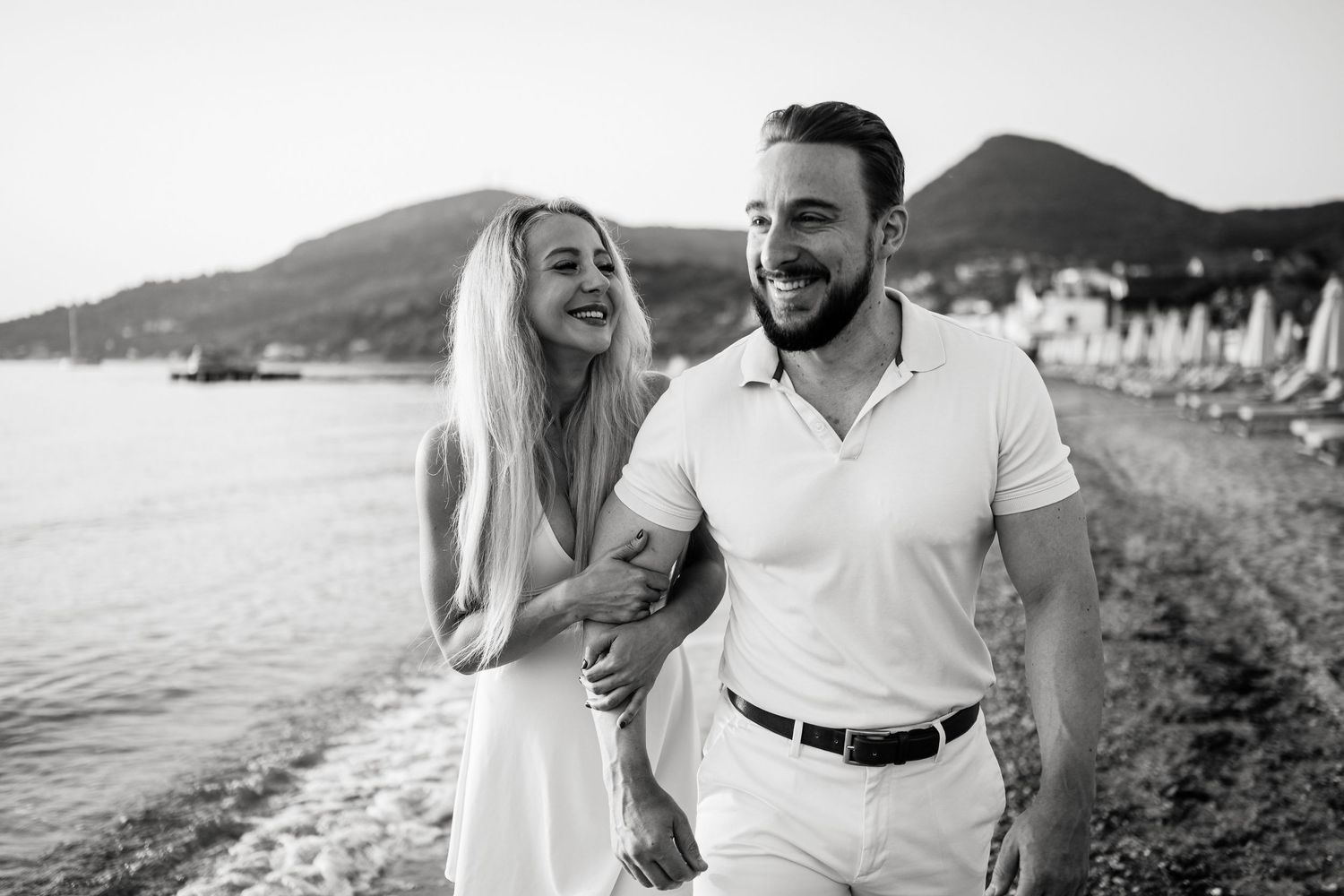 Couple in white outfits enjoying a romantic moment by the seaside.