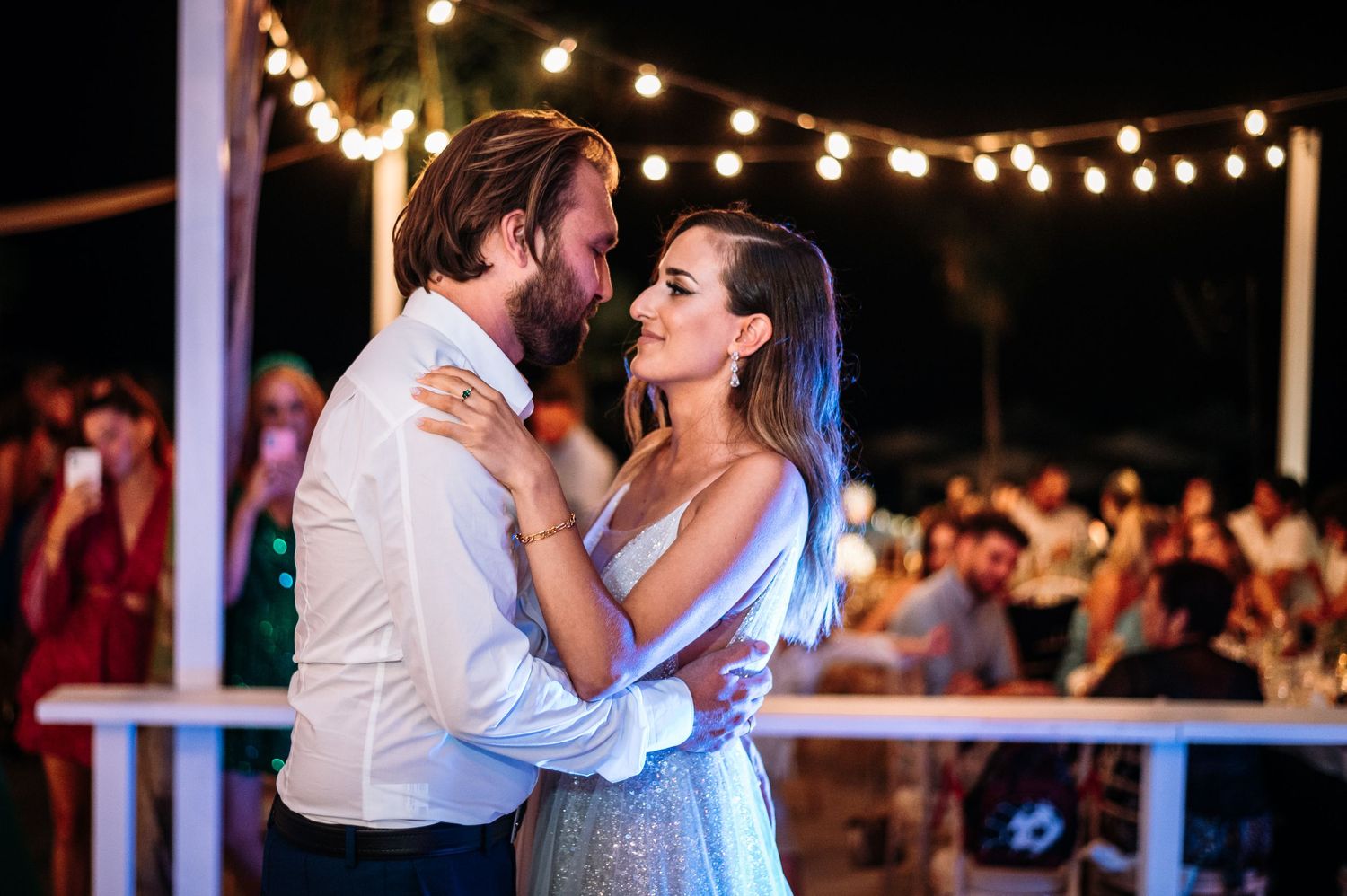 Couples dancing together at a festive outdoor wedding reception with string lights overhead.