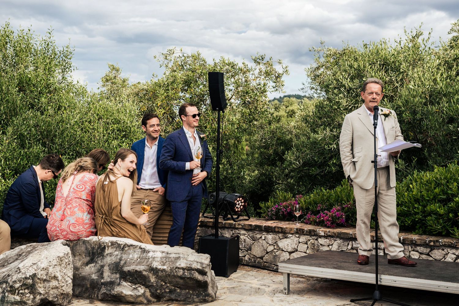 Outdoor wedding ceremony taking place on a stone patio surrounded by lush greenery.