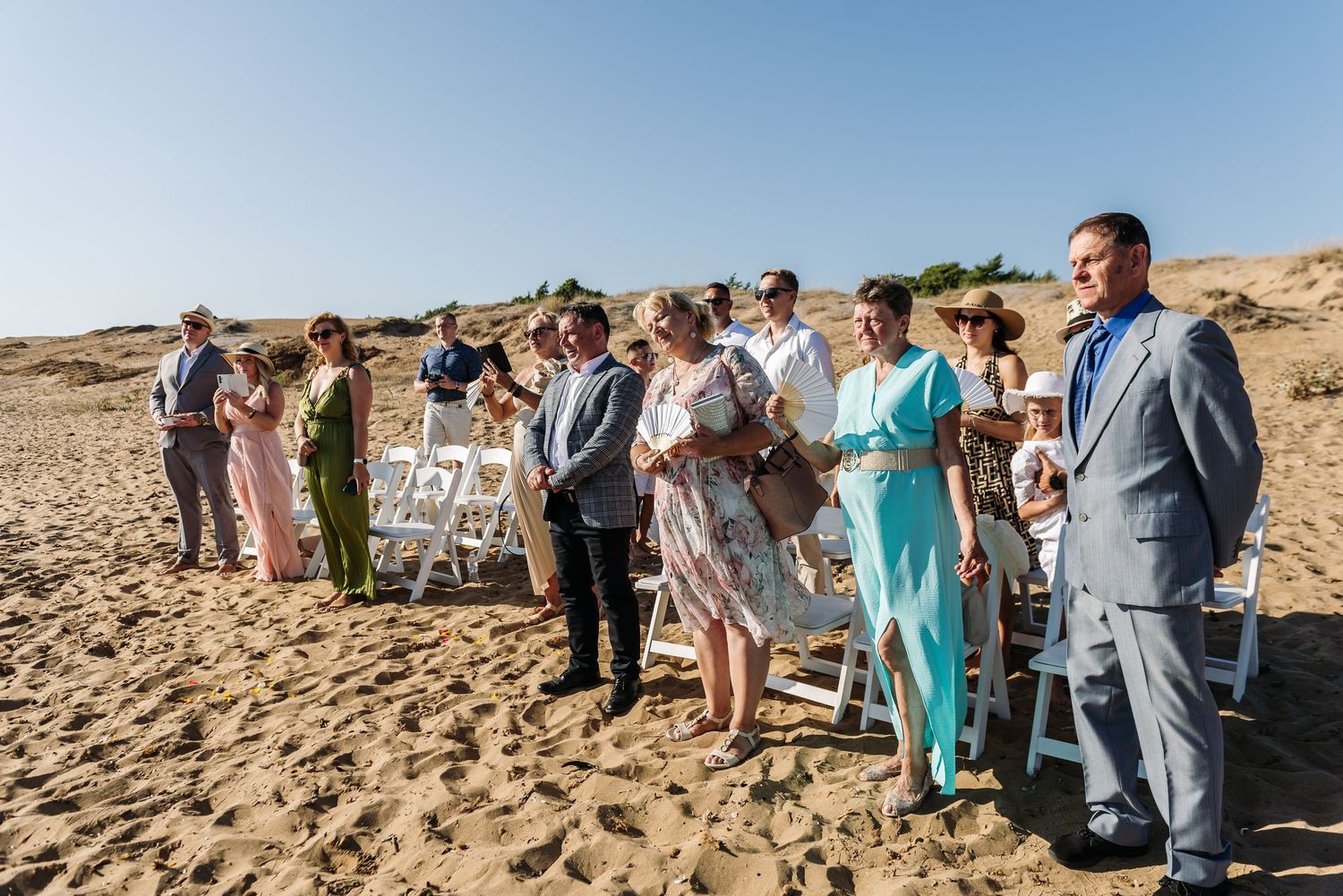 Wedding guests gathered on sandy beach during outdoor ceremony.
