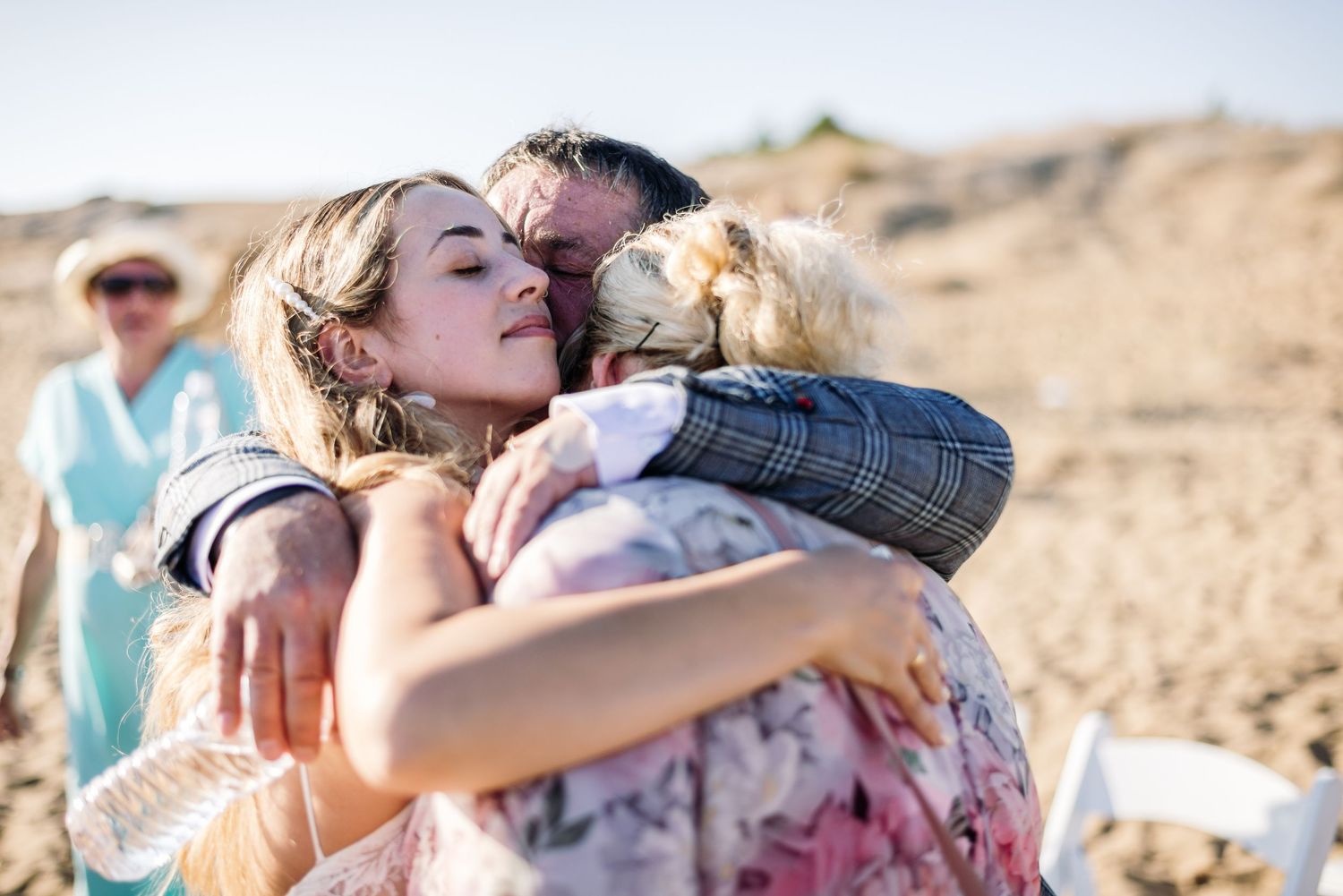 Wedding guests sharing emotional embraces after beach ceremony.
