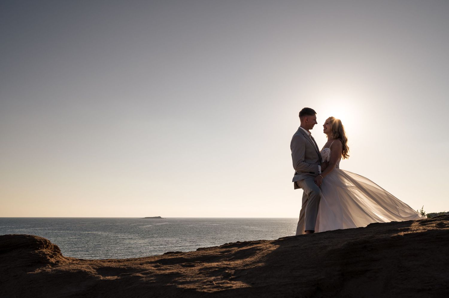 Silhouetted coastal wedding photography with dramatic sunset lighting.