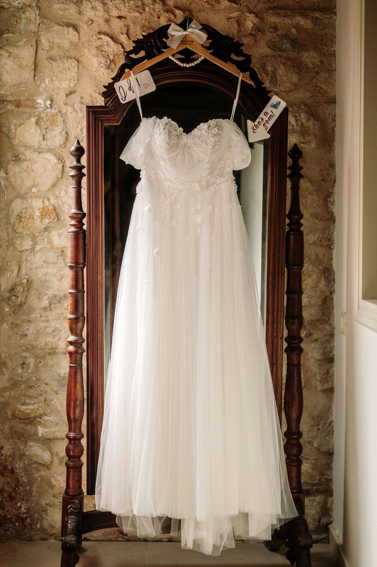 White flower girl or communion dress displayed on hanger against rustic stone wall.
