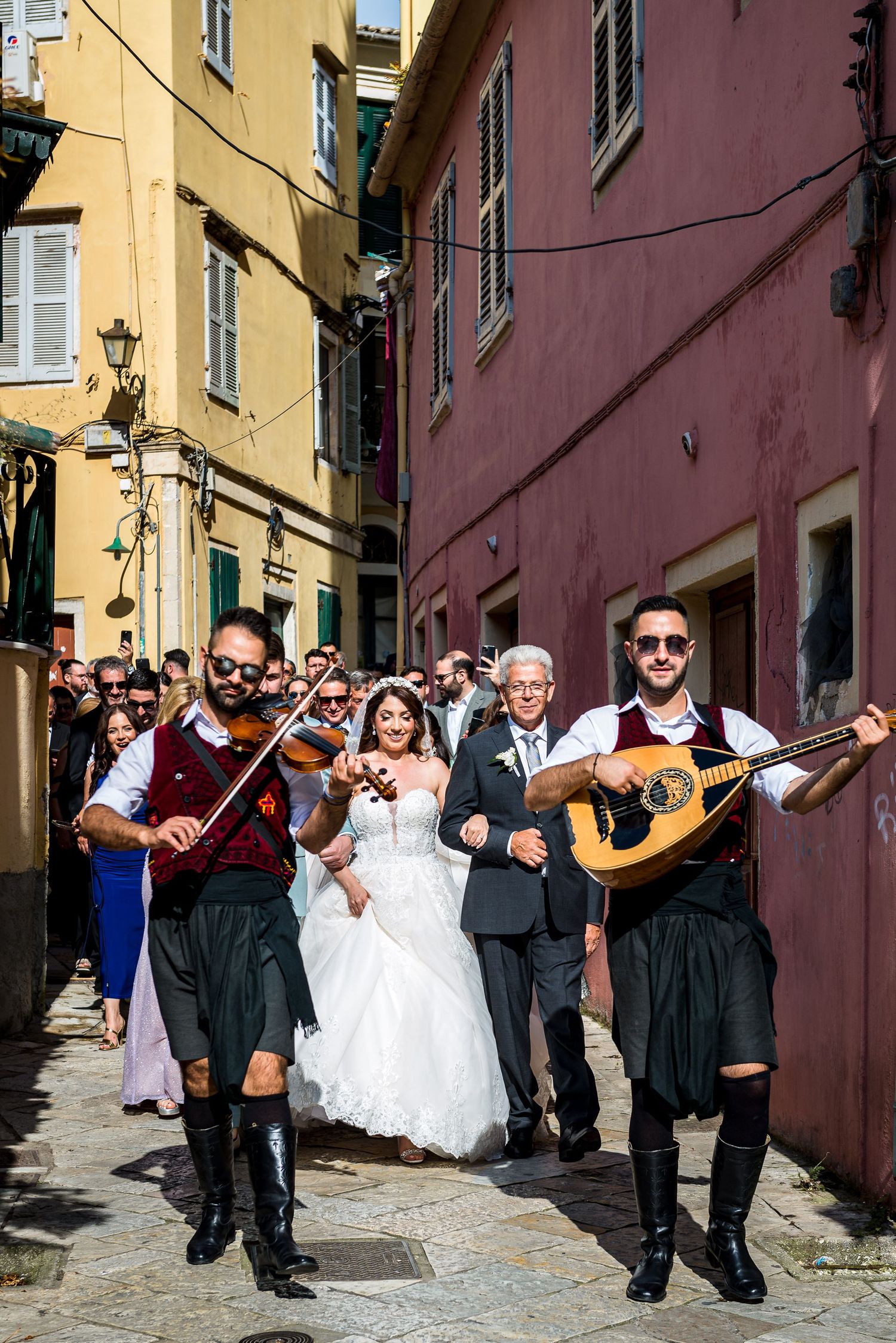 Wedding procession through narrow Italian streets with musicians and guests following the couple.