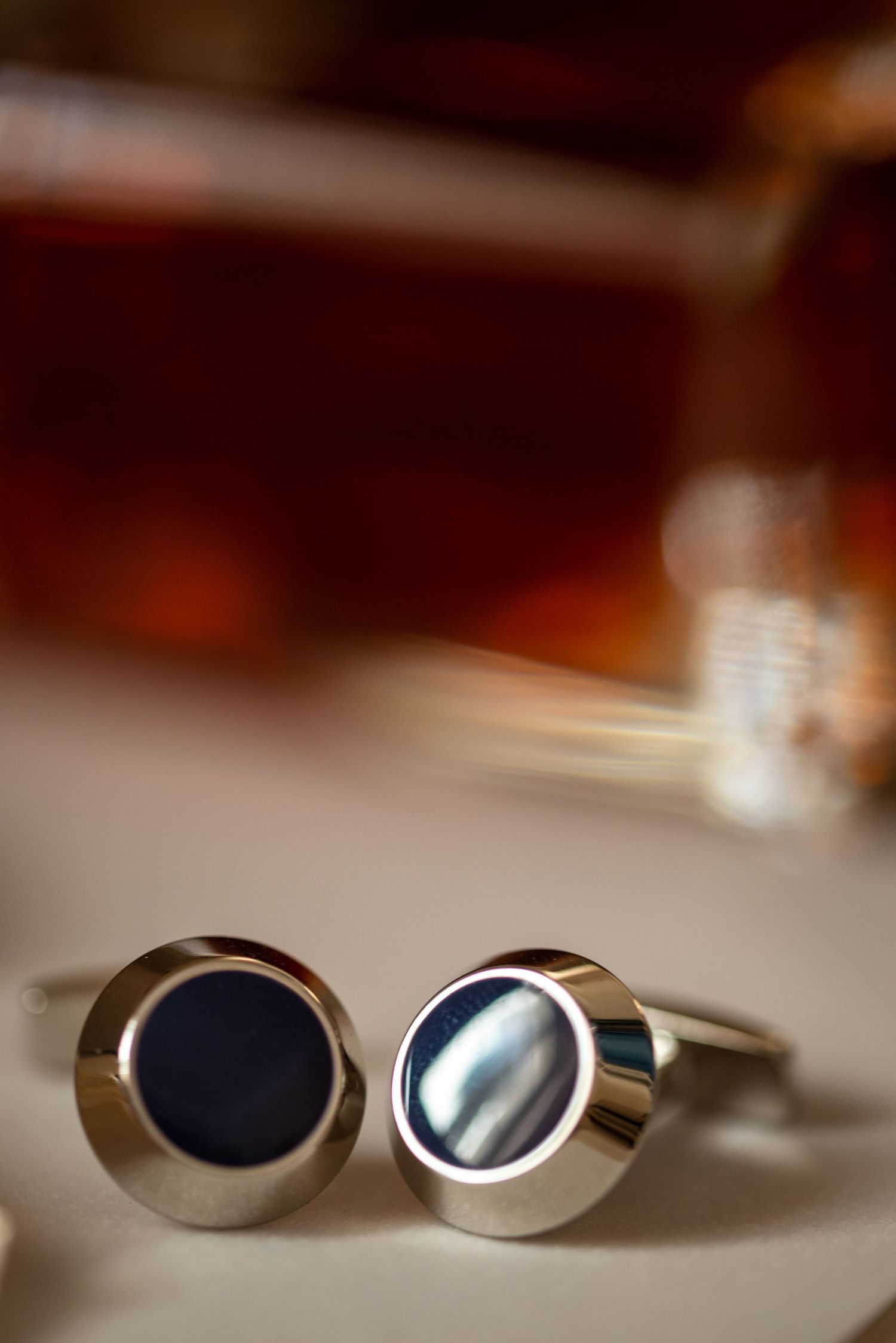 Close-up of silver cufflinks with dark navy centers on reflective surface.