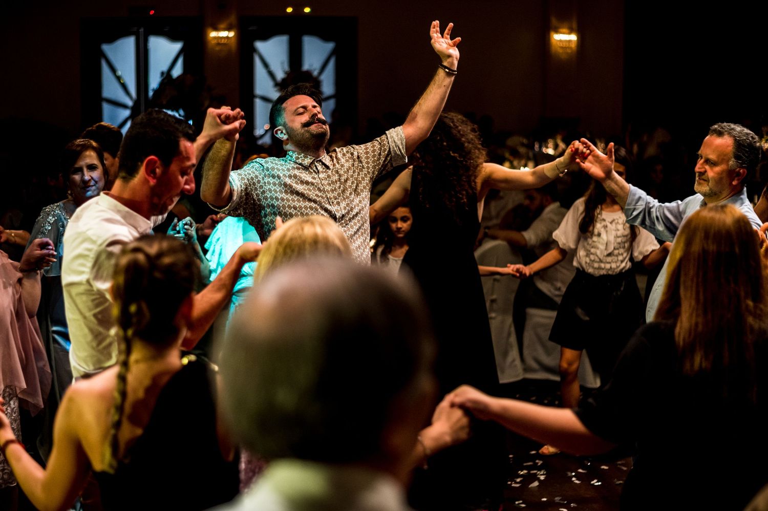 Wedding celebration with guests dancing energetically in a dark reception venue.