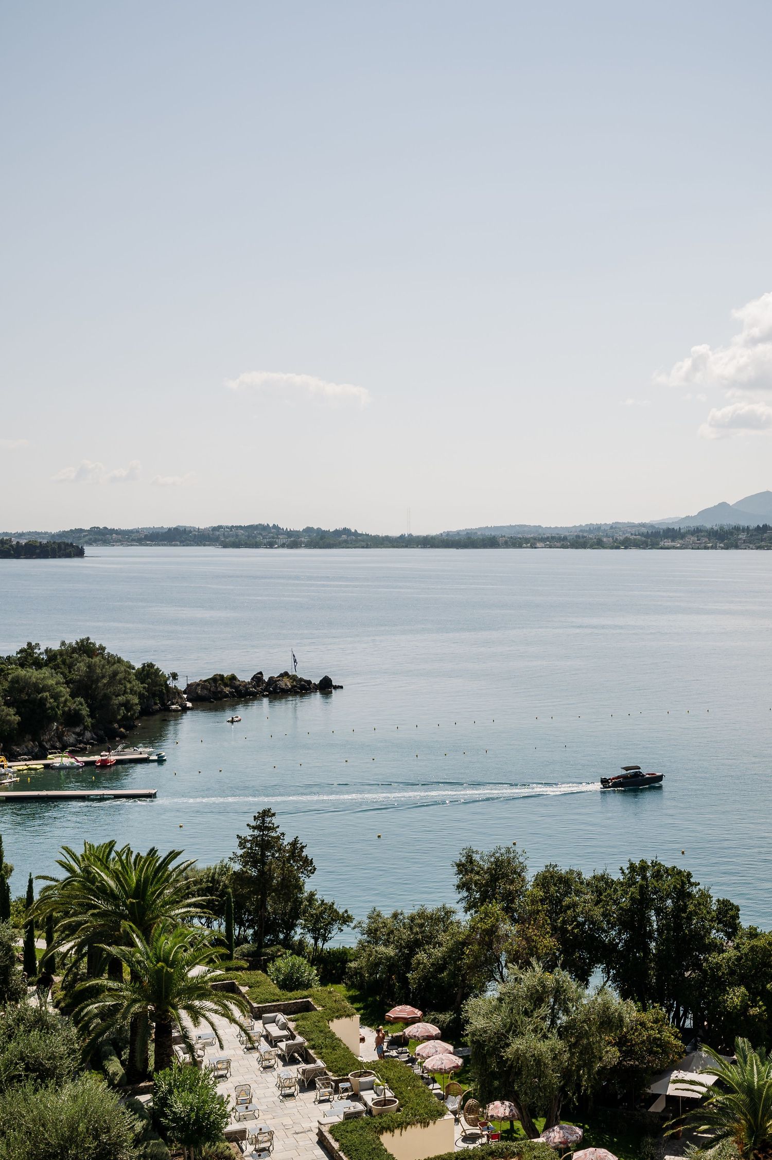 Scenic coastal view of a Mediterranean bay with palm trees and boats in calm waters.