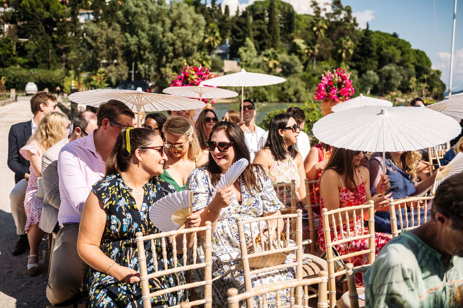 Outdoor wedding ceremony setup with wooden chairs and guests under blue sky.