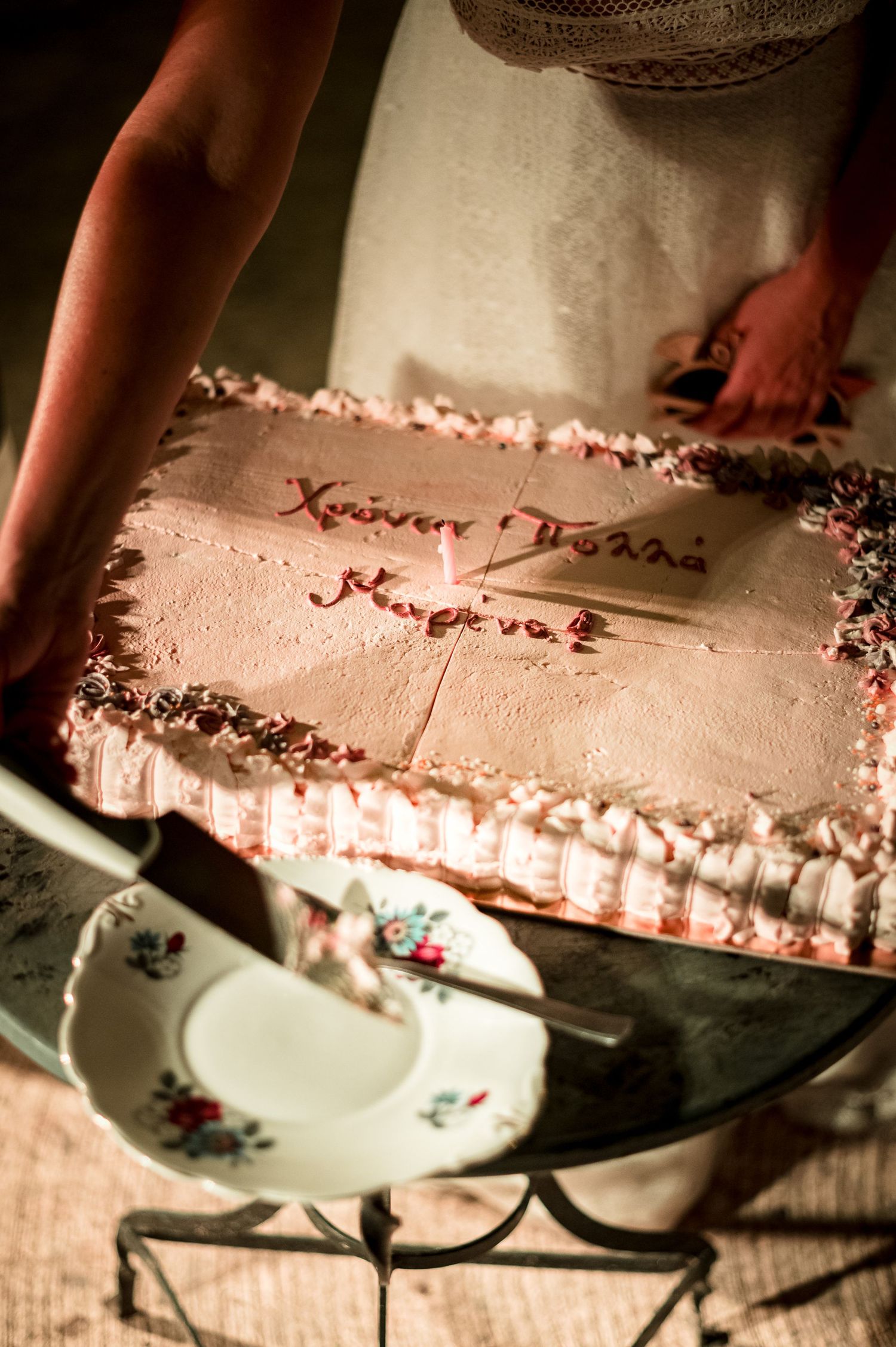 Close-up view of pink frosted cake being decorated with delicate piping details.