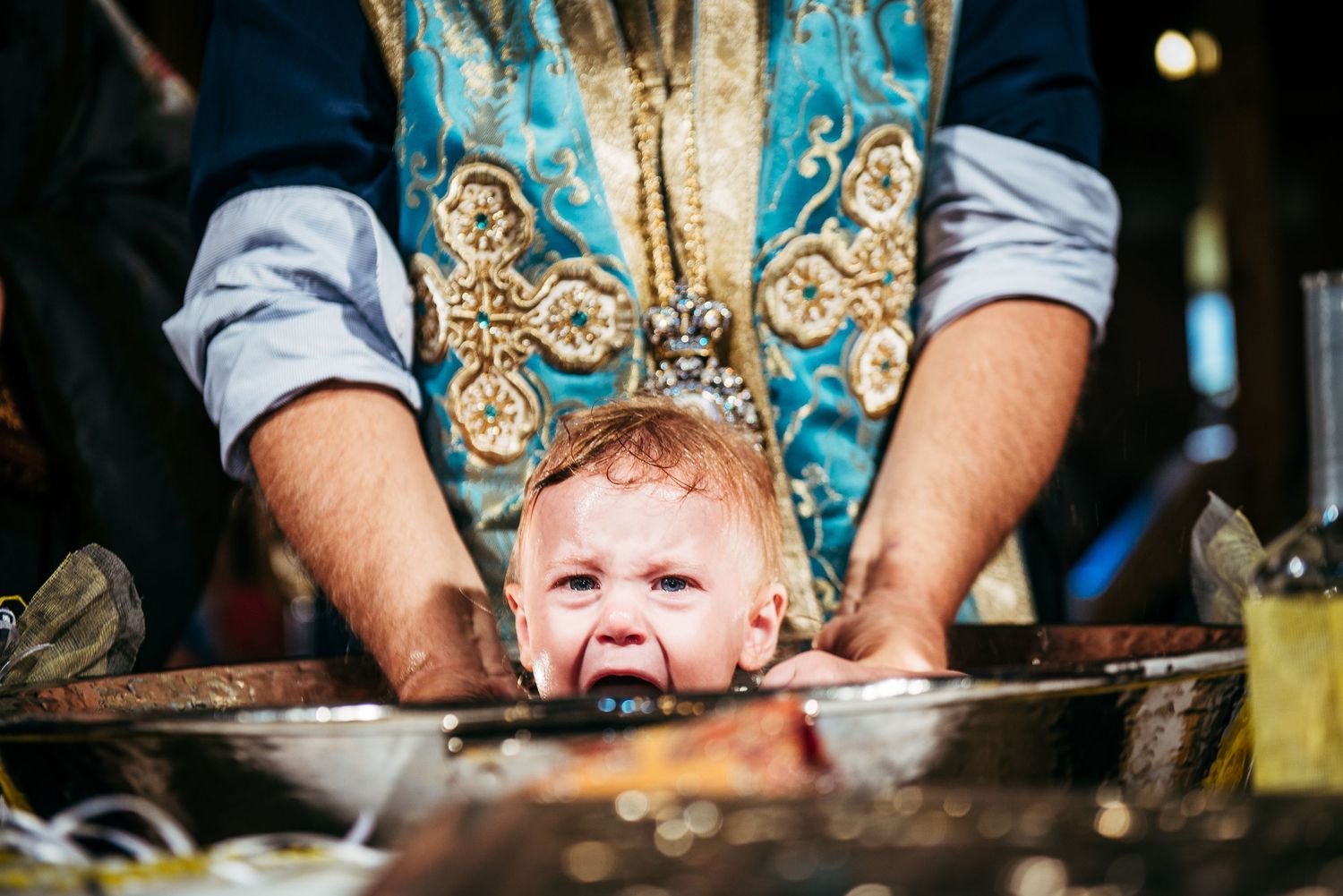 Close-up sequence of baby in ornate baptismal gown being held over ceremonial font.