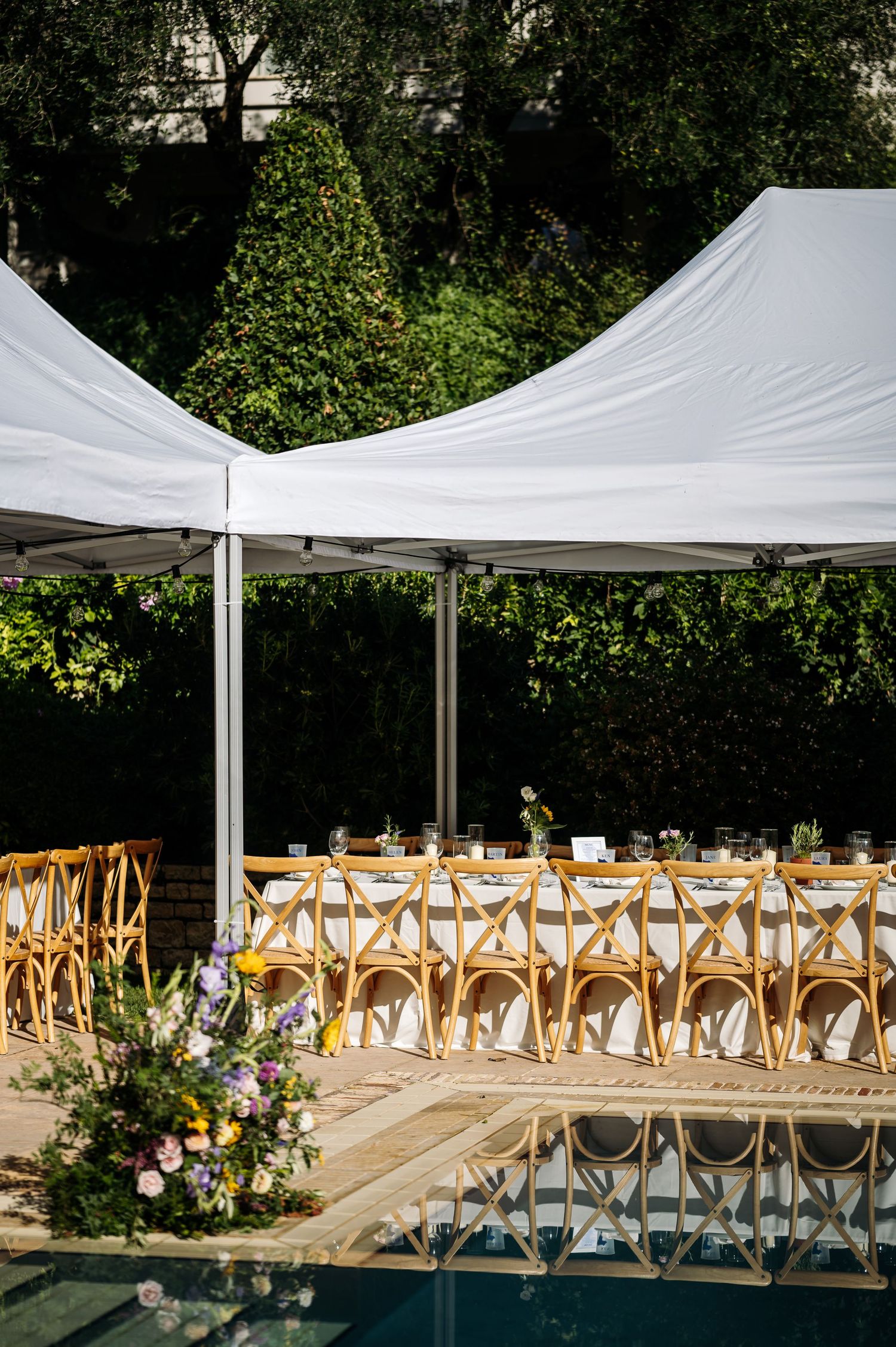 White tent canopies and wooden cross-back chairs set up for an elegant outdoor wedding ceremony.