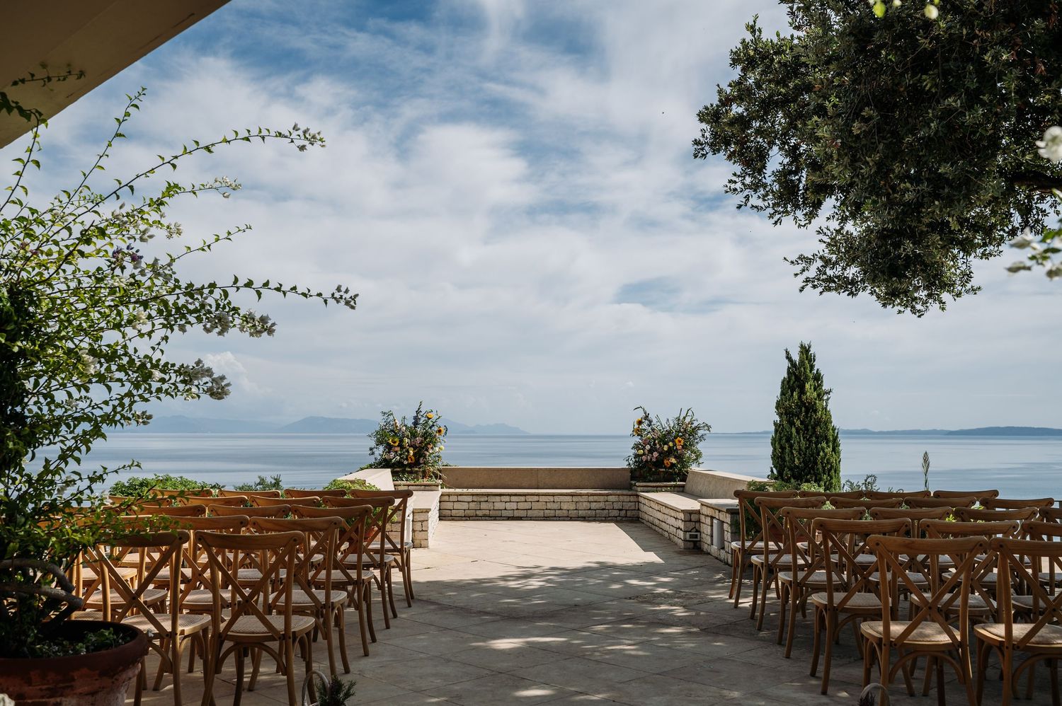 Wooden cross-back chairs arranged in rows for an outdoor ceremony with ocean views and blue skies.