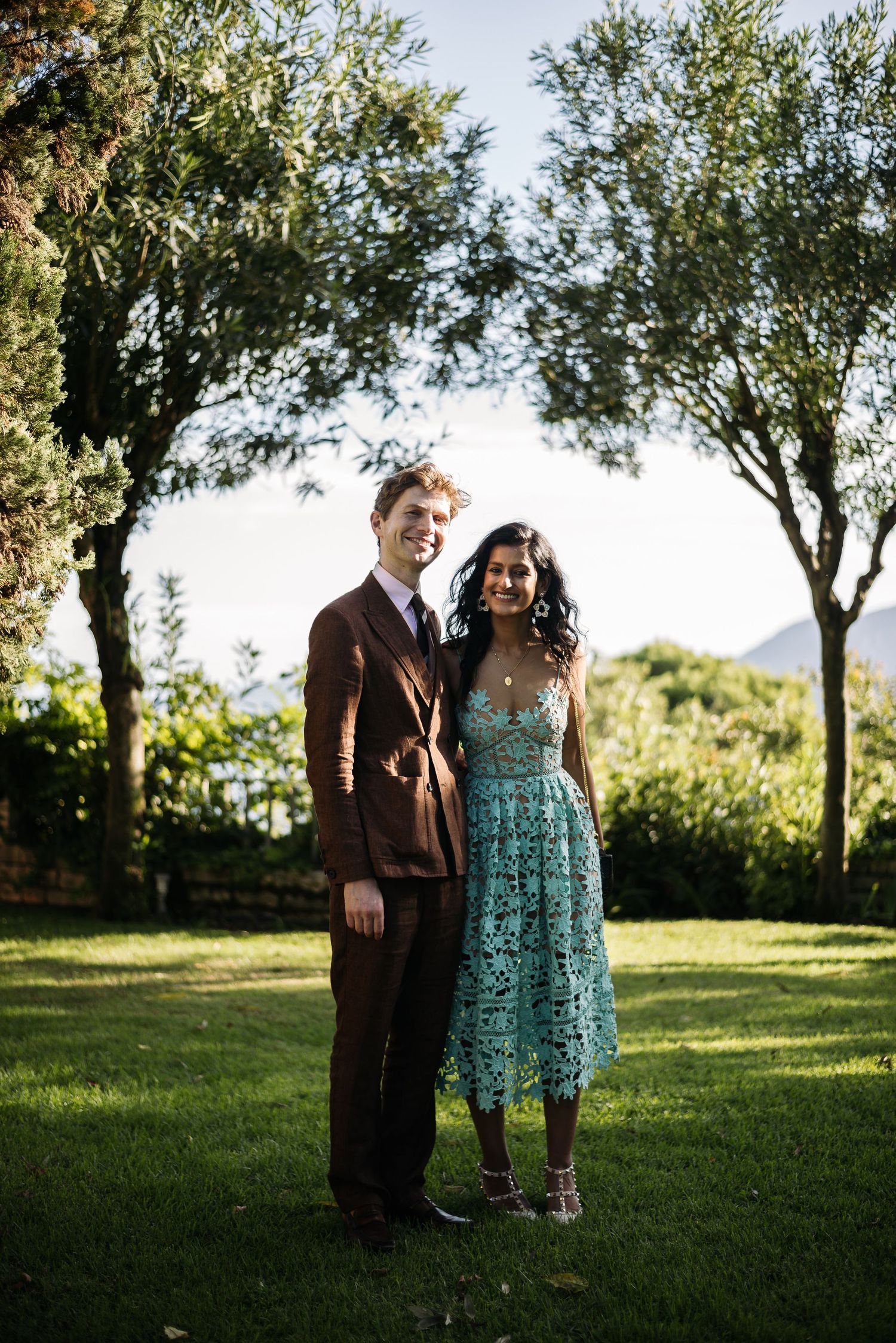Couple sharing a tender moment on grassy lawn with trees in background during golden hour.