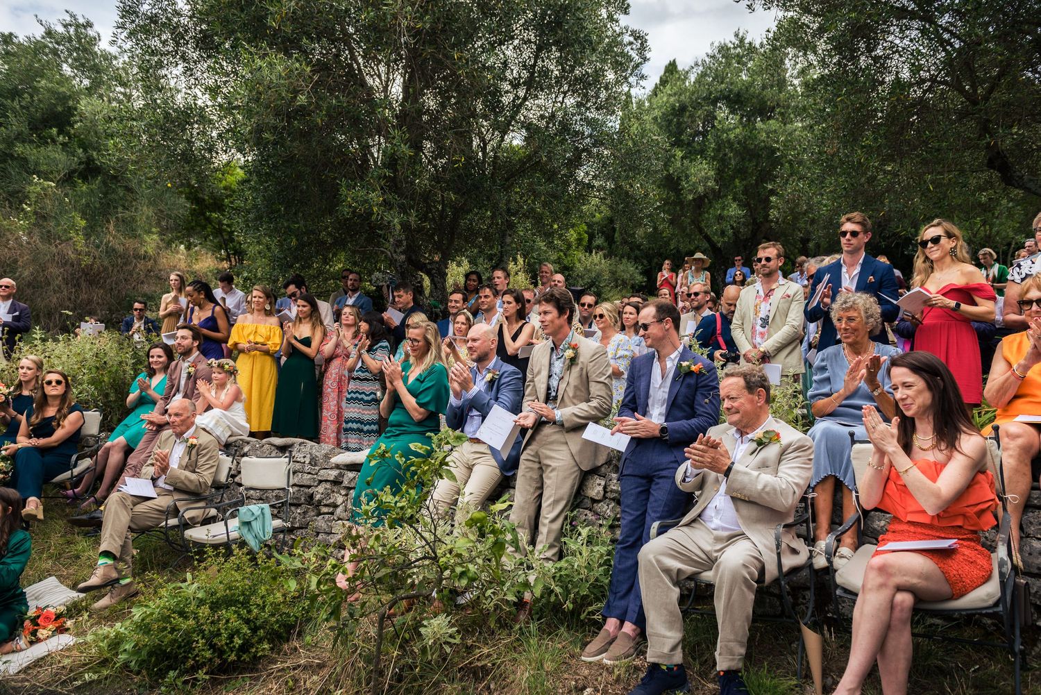 Wide angle shot of wedding guests seated in rows at an outdoor venue.