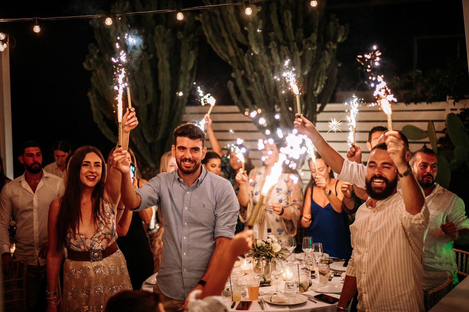 Festive nighttime celebration with sparklers and string lights.