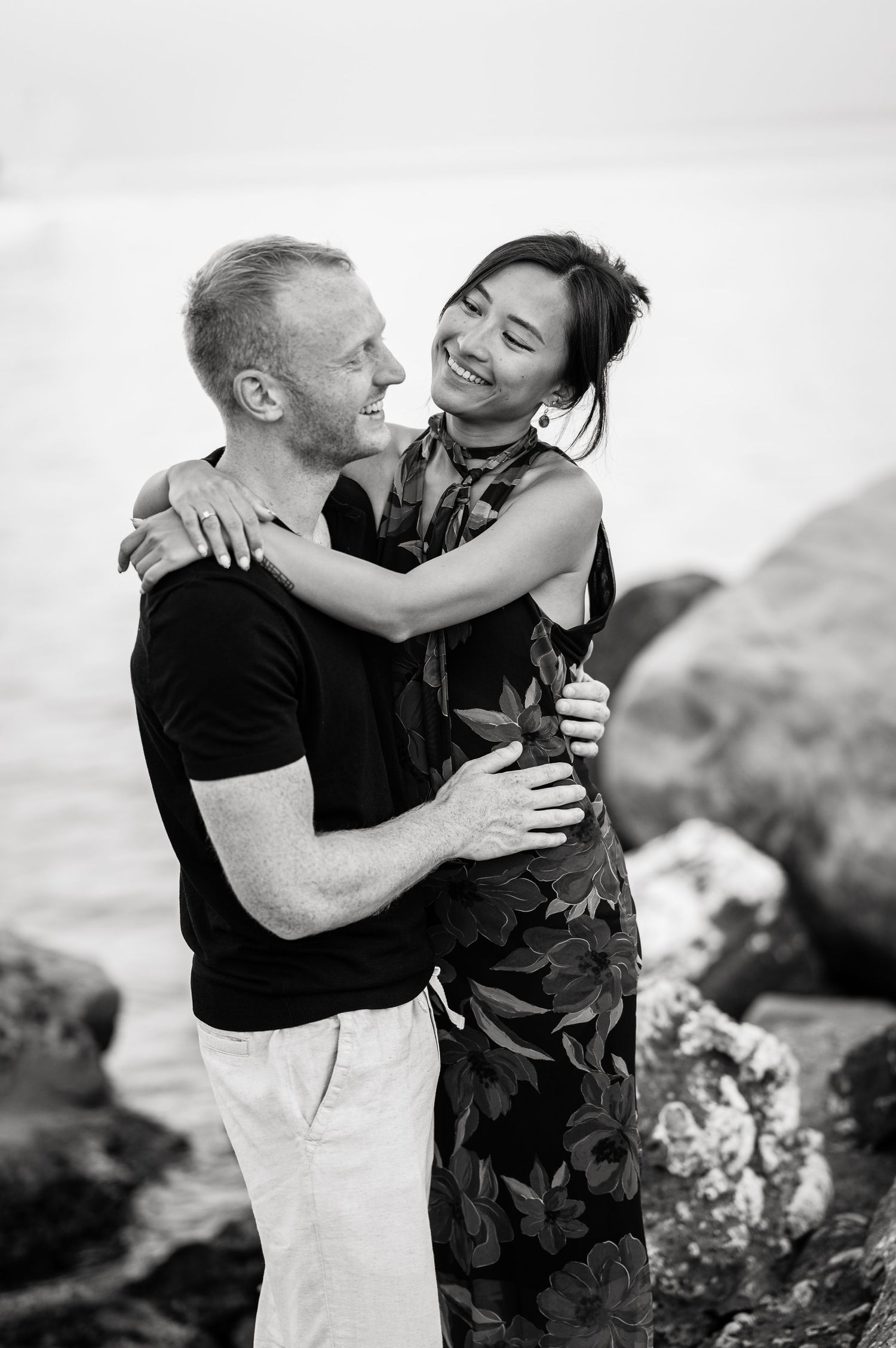 A black and white portrait of a couple laughing and embracing outdoors.