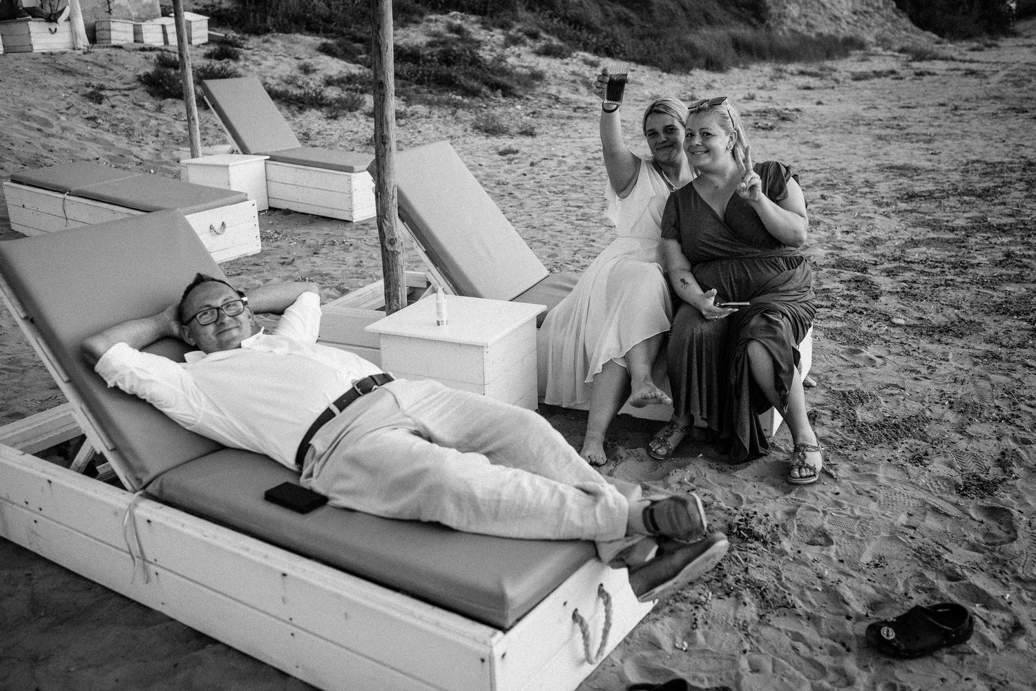 Wedding guests relax on lounge chairs at a beachside reception.