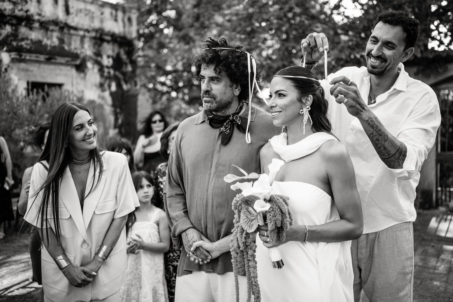 Black and white photo captures candid moments between wedding guests during outdoor celebration.
