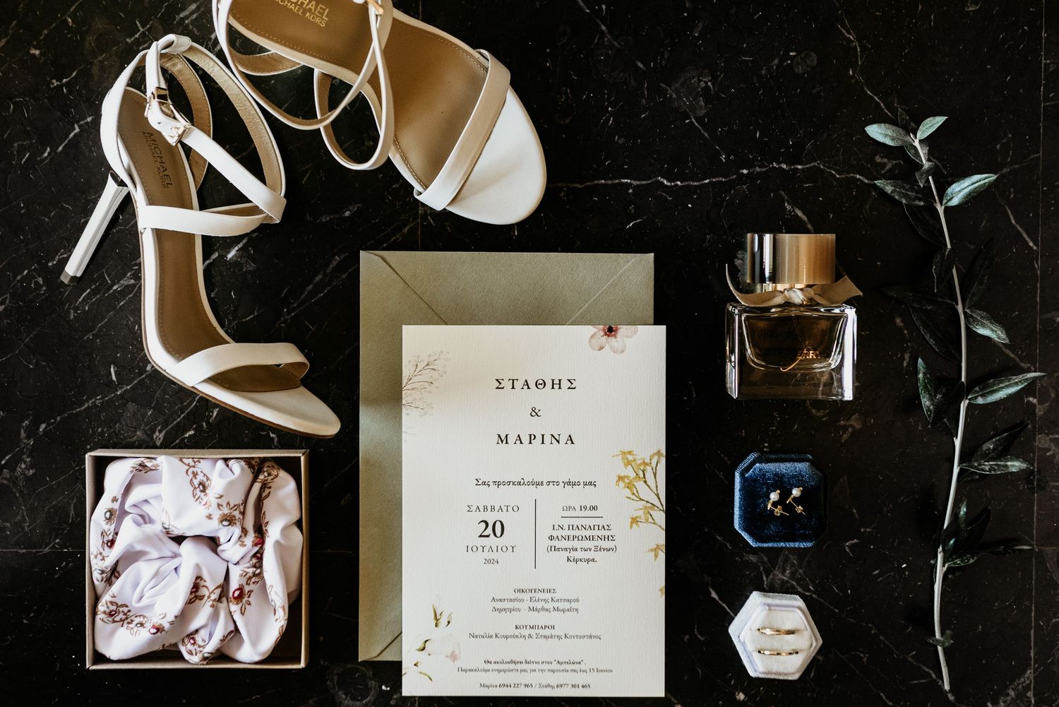 Wedding details flatlay with invitations, perfume, and accessories on dark background.