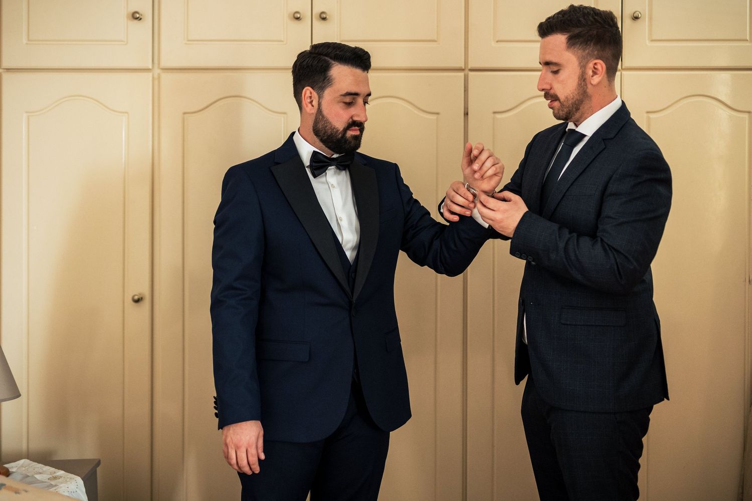Groomsmen in black tuxedos sharing candid moments before the wedding ceremony.