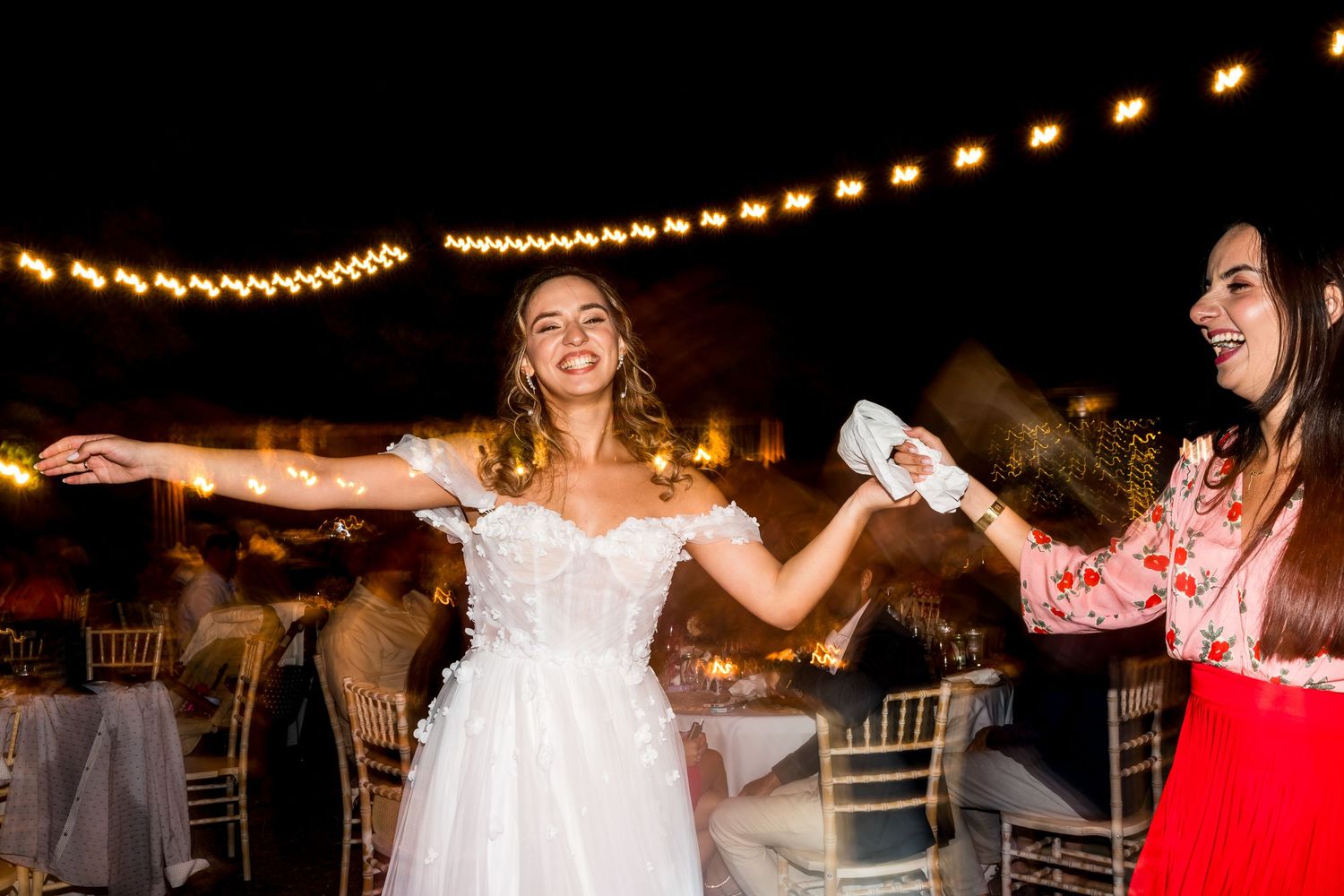 Wedding guests dance and celebrate under string lights at outdoor reception.