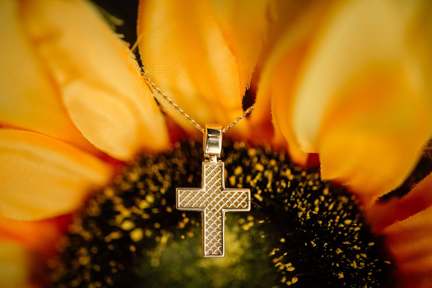 Close-up of silver cross pendant necklace against vibrant sunflower petals.