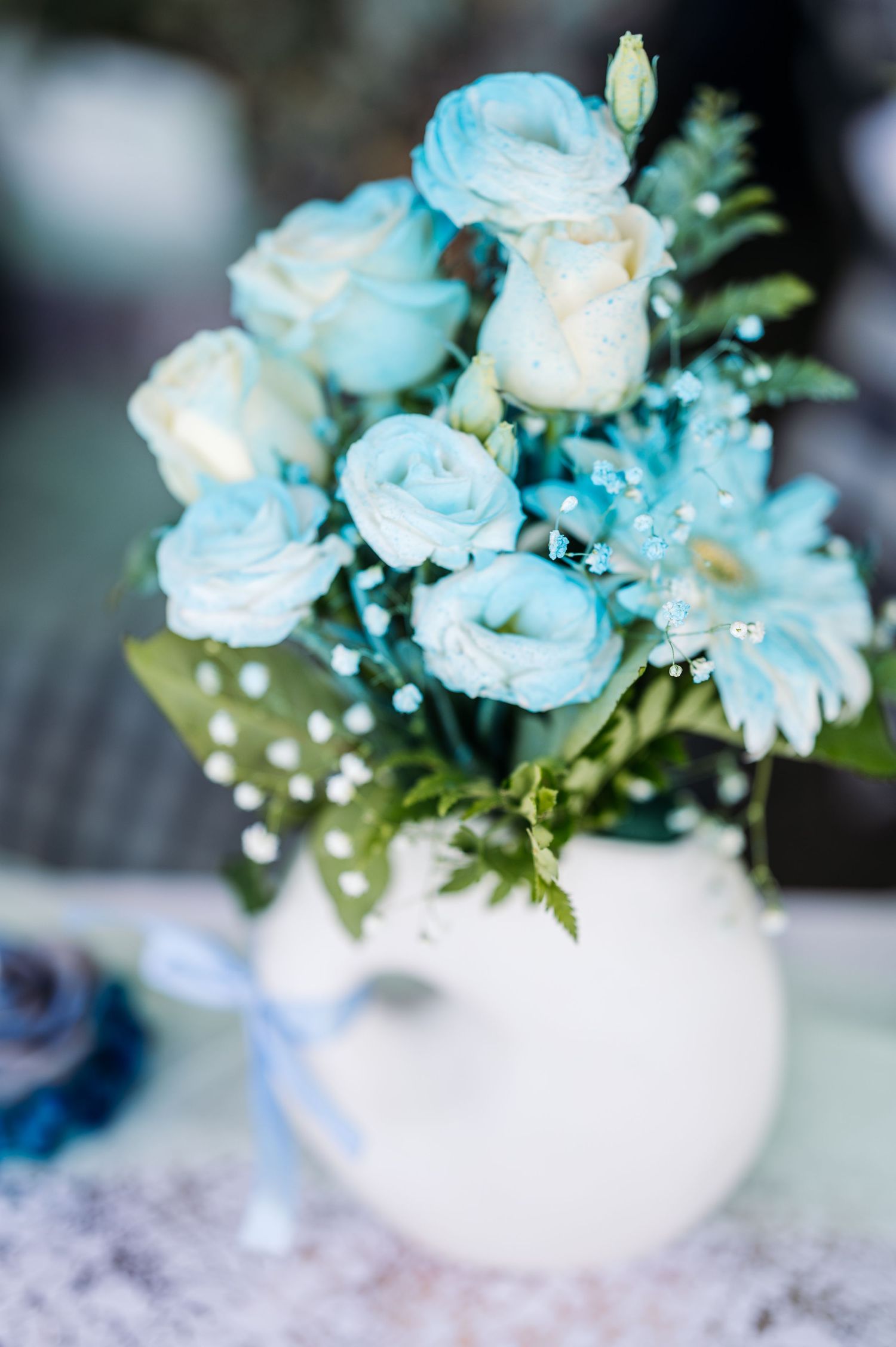 Delicate light blue and white roses arranged in a white vase with baby's breath accents.