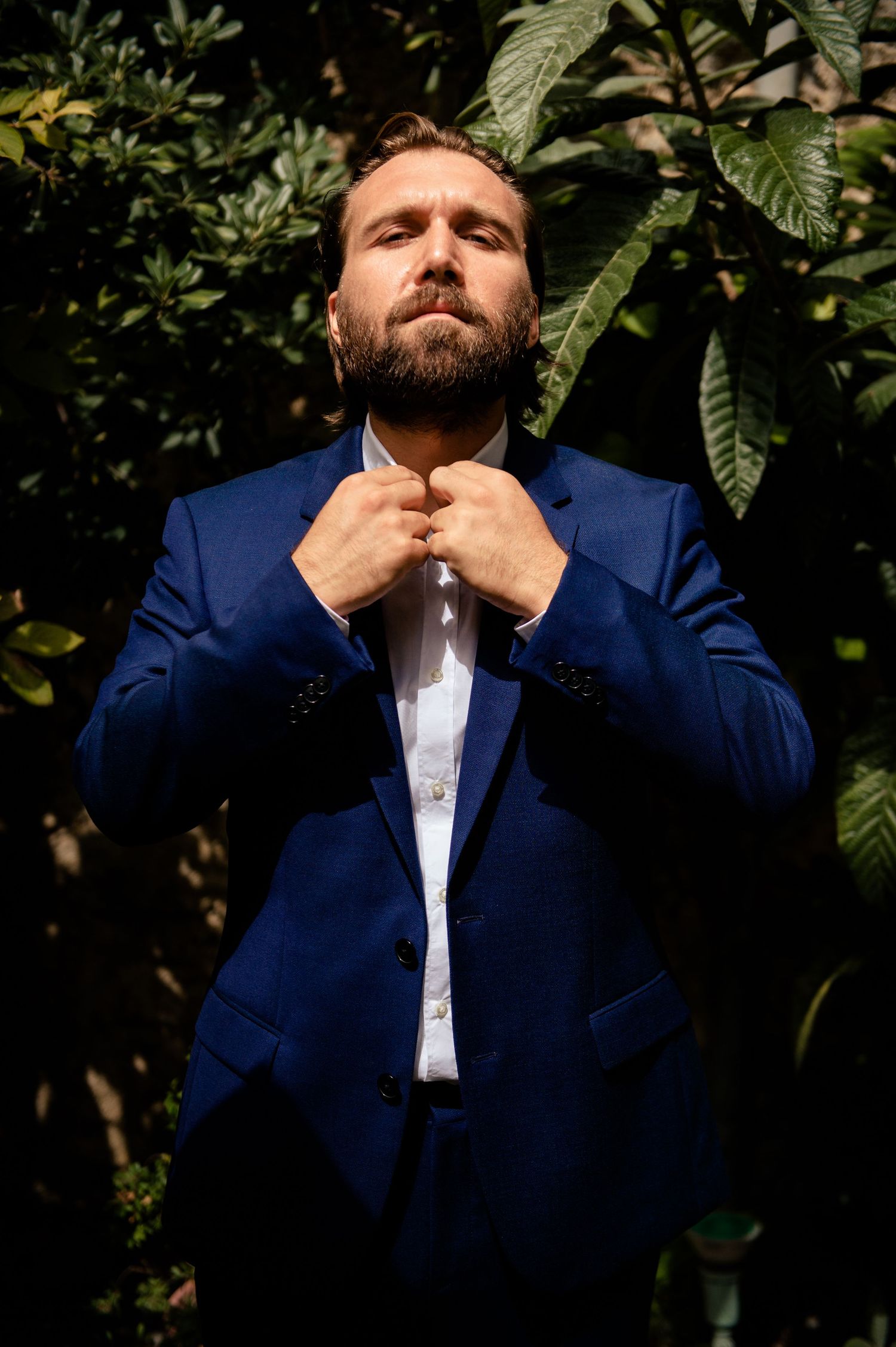 Series of shots showing someone adjusting a navy suit and tie against green foliage.