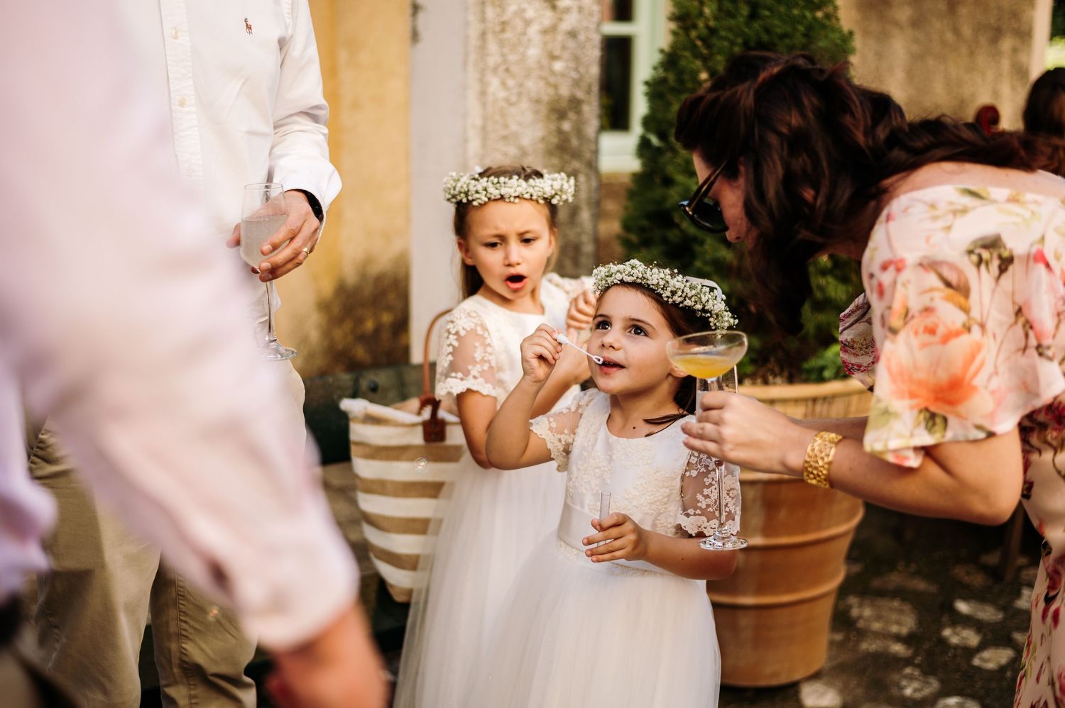 Young flower girls in white dresses and crowns look up with wonder during a wedding ceremony.