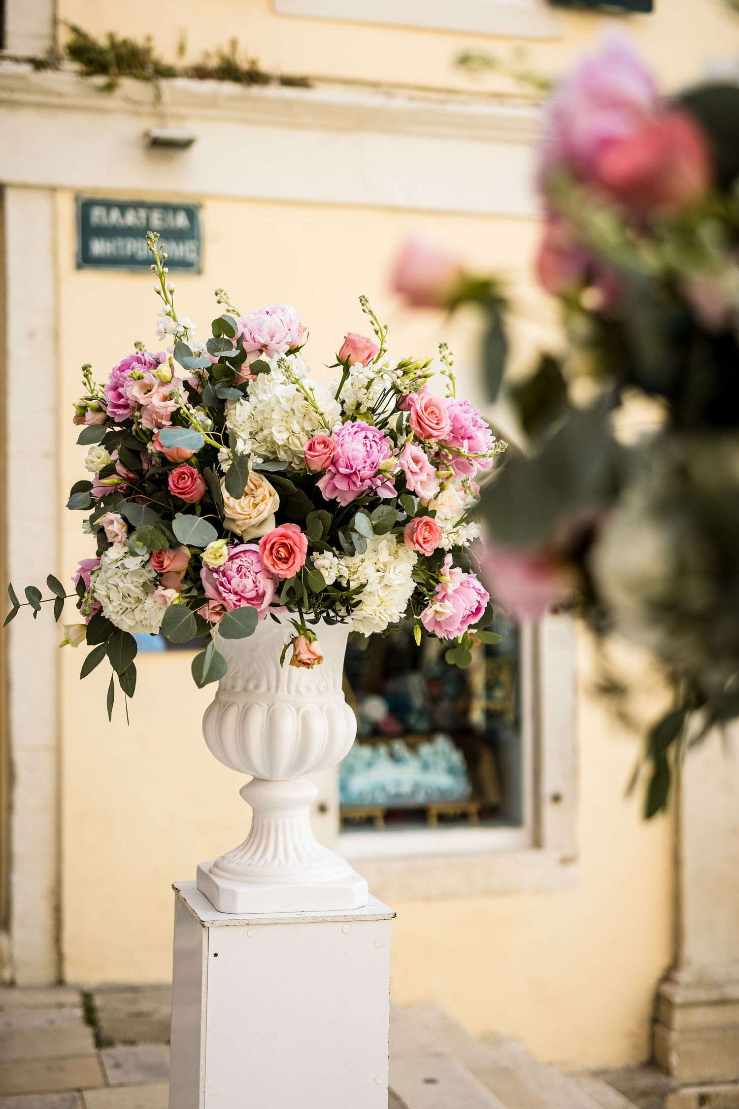 Elegant floral arrangements in white vases featuring pink and white roses against a cream-colored wall.