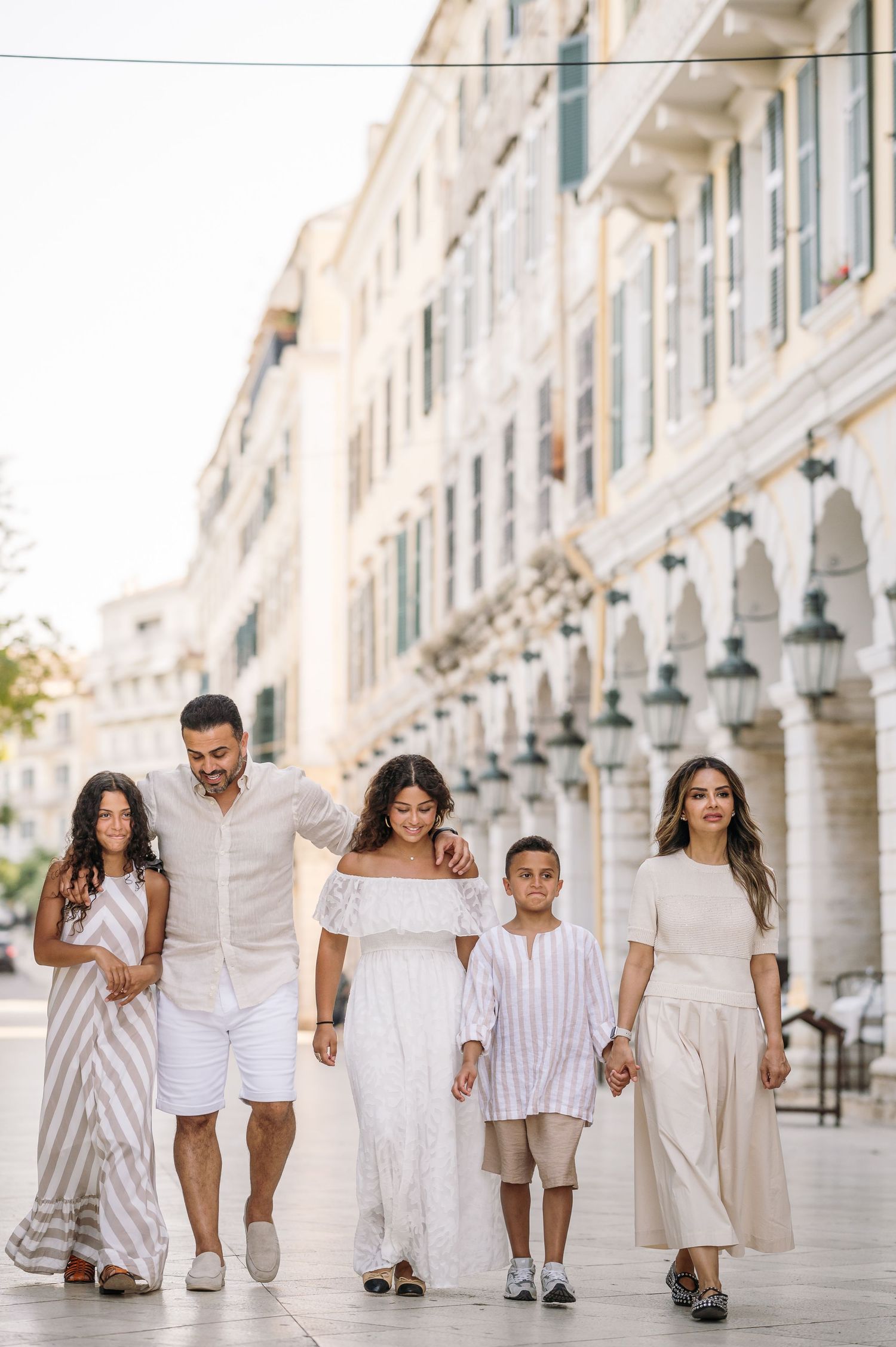 Family dressed in white and beige outfits walking together along a beautiful colonnade walkway.