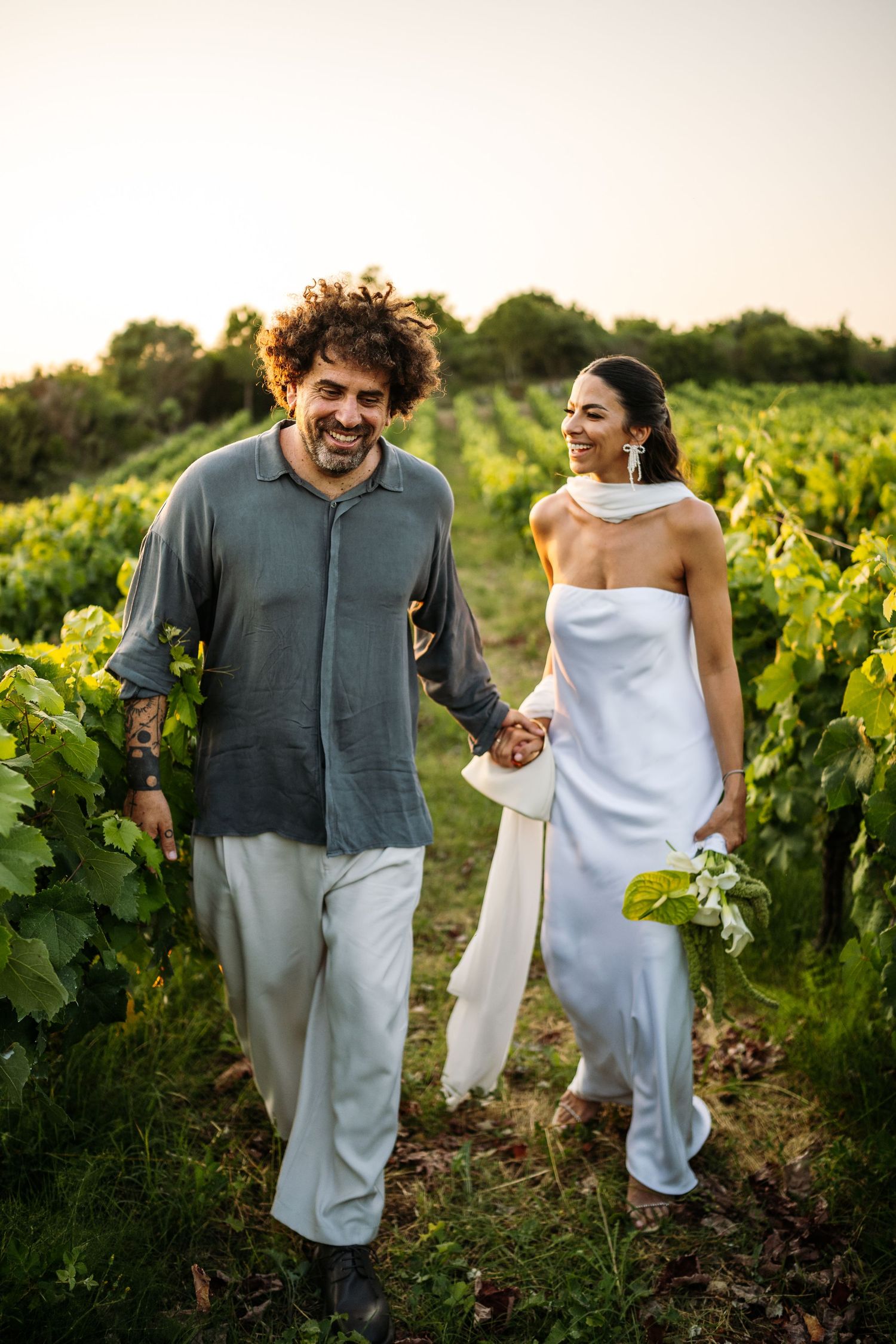 A couple shares joyful moments together while walking through a sunlit vineyard at sunset.