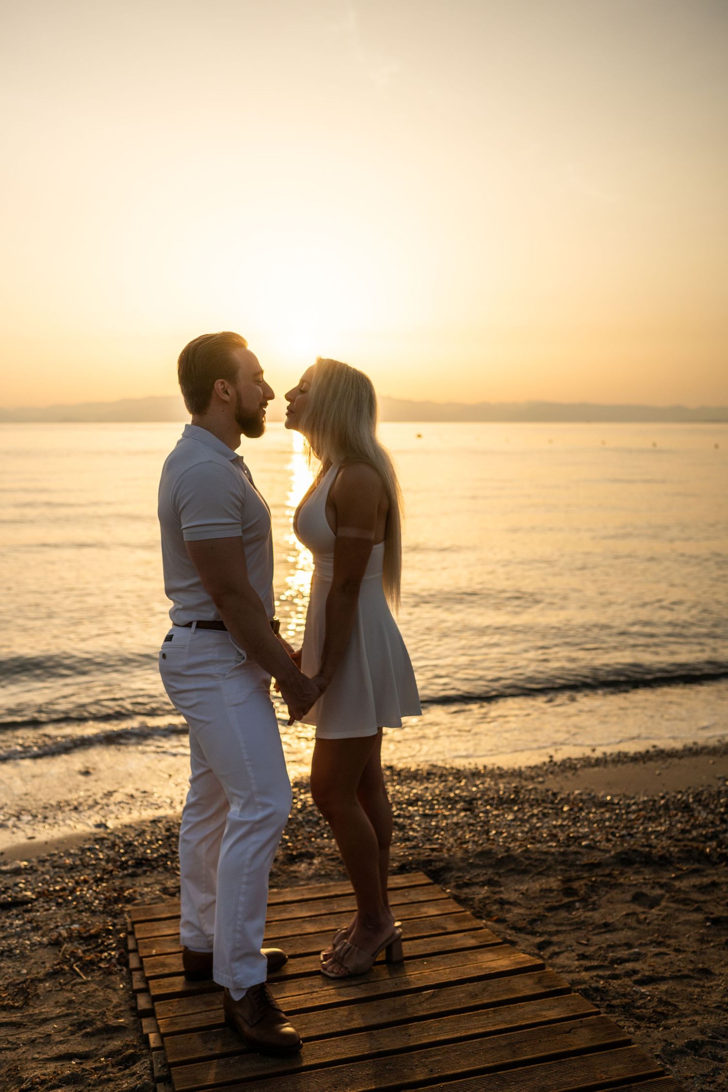 Romantic couple sharing an intimate moment on wooden boardwalk at beach during sunset.